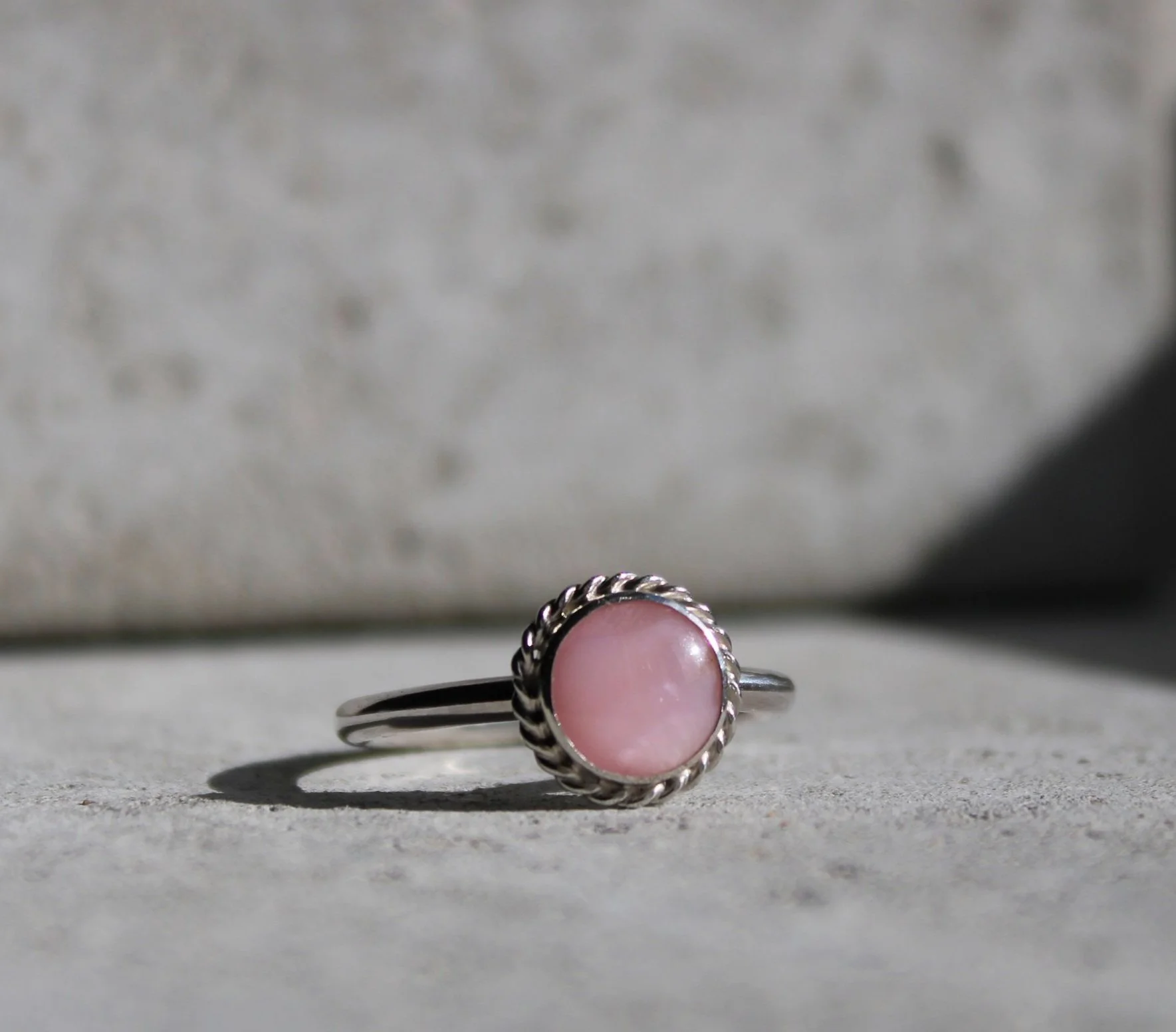 A silver ring with a pink gemstone set in a twisted metal bezel.