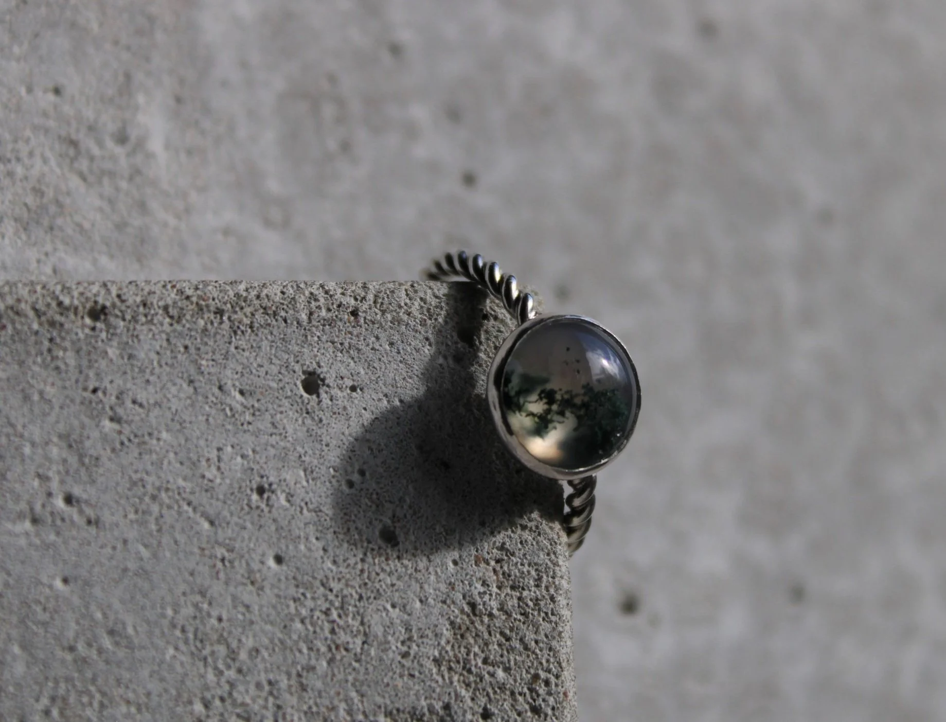 A silver ring with a round, reflective black stone, resting on a textured concrete surface.
