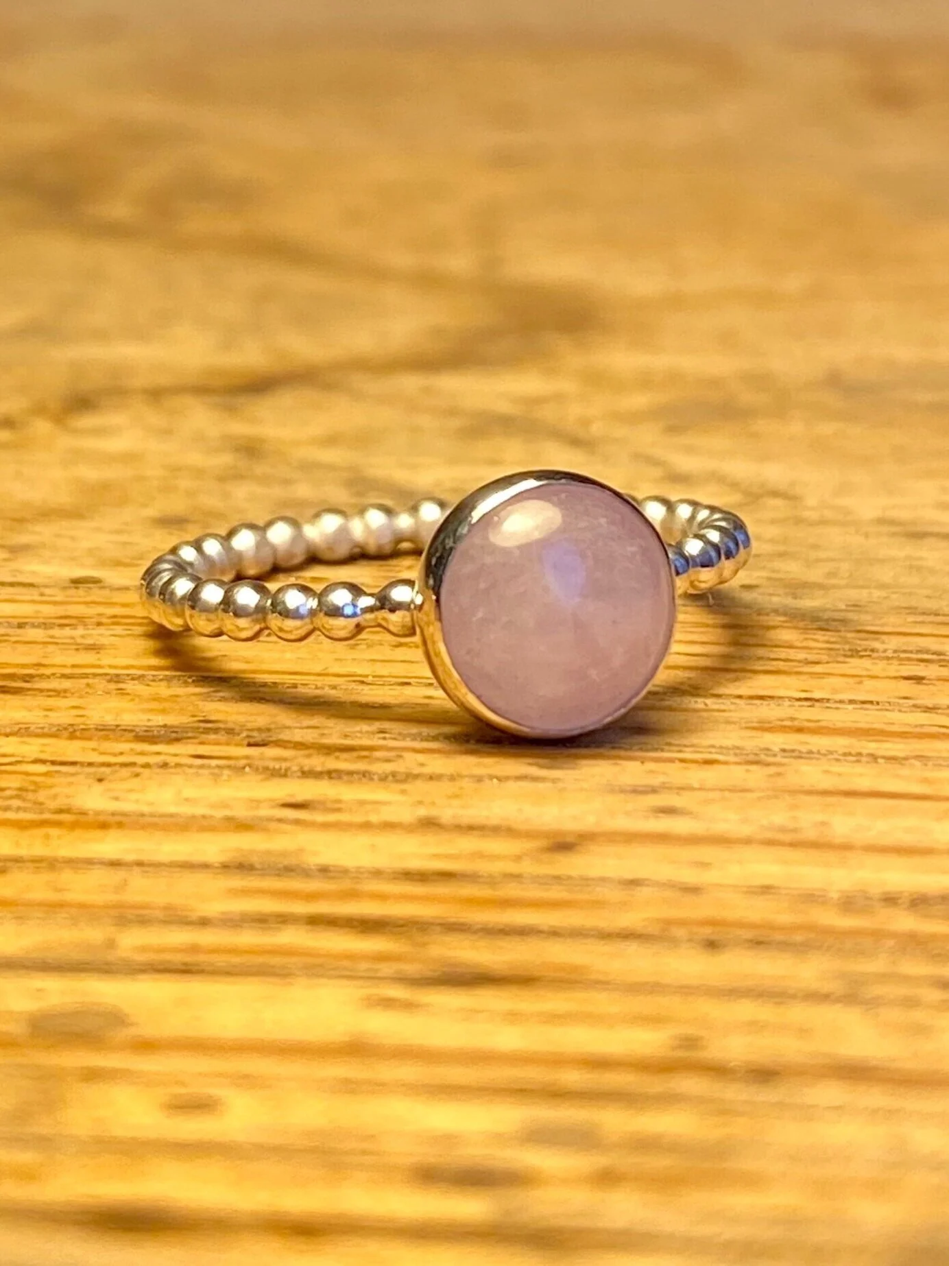 A silver ring with a round, pink gemstone on a wooden surface.