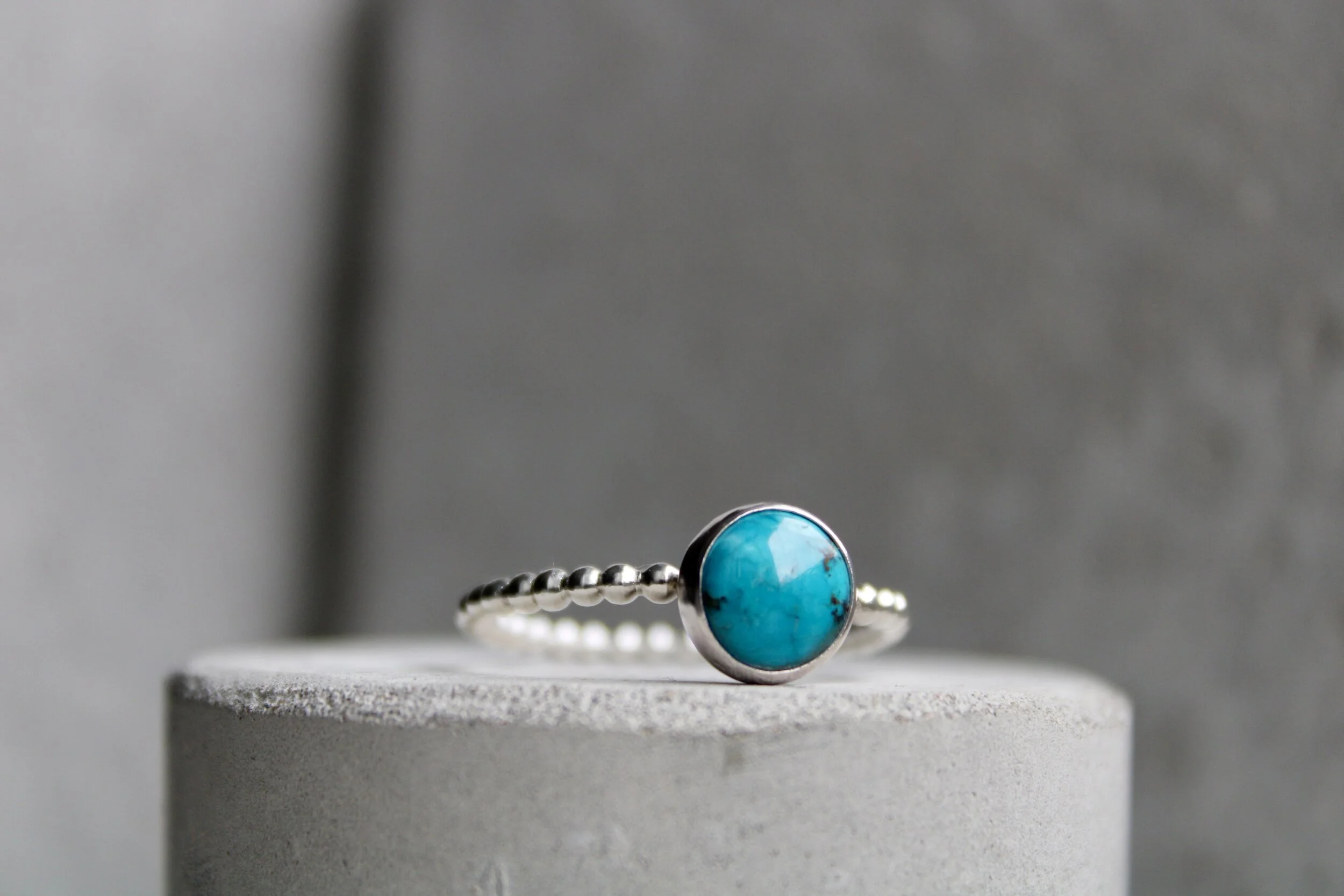 Silver ring with a round turquoise stone on a gray surface with a gray background.