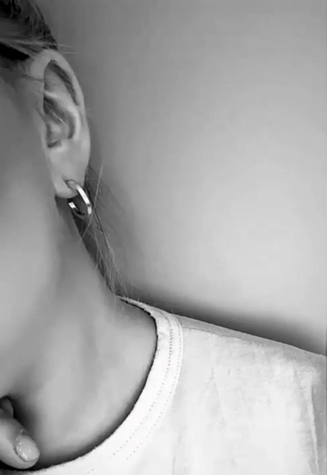 Close-up of a woman's face turned away, showing her ear with a hoop earring, part of her neck, and shoulder with a white shirt.