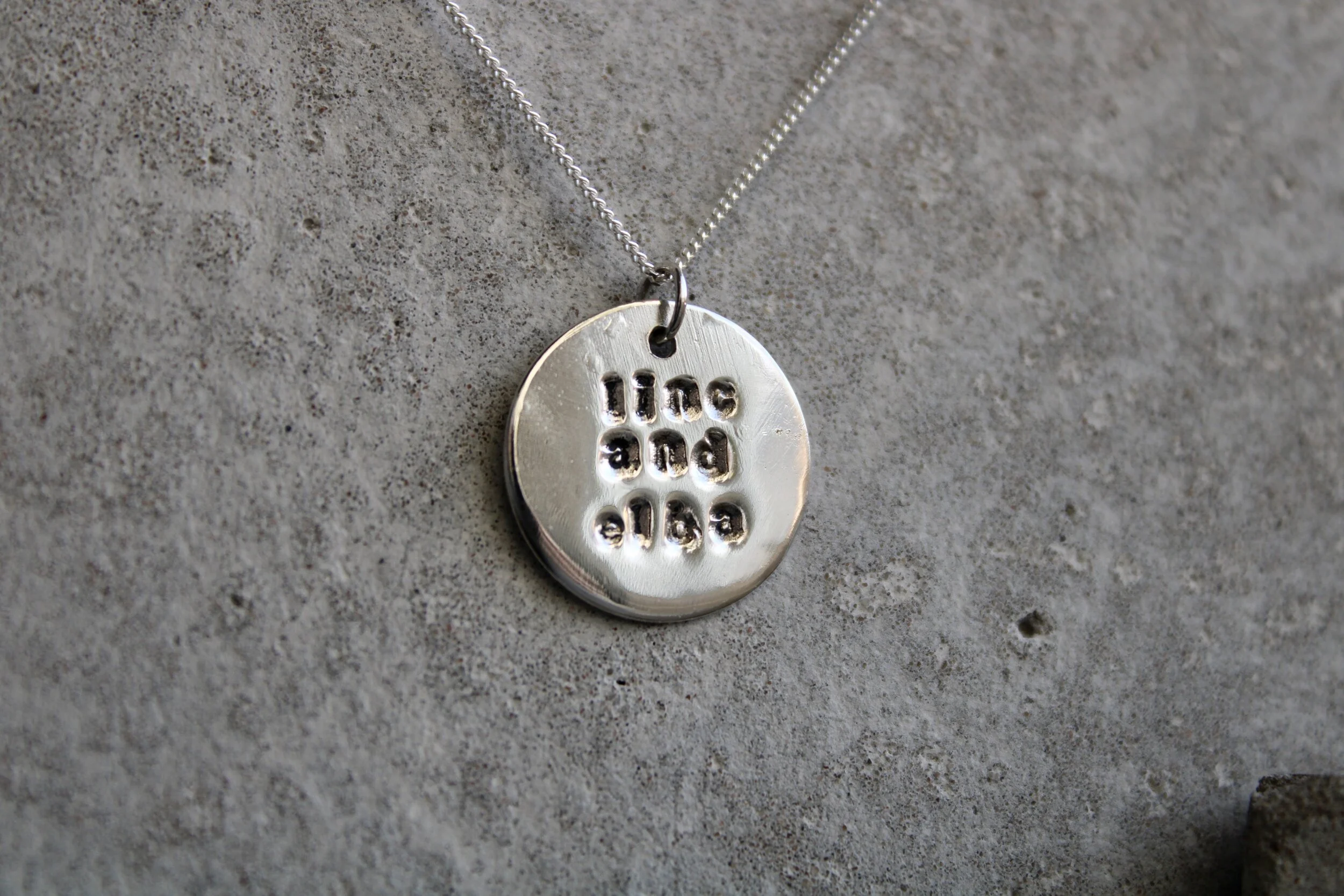 Silver pendant necklace with the phrase "Celle and bill" engraved in a circular shape.