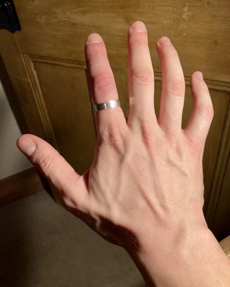 A hand with a silver ring on the middle finger, positioned in front of a wooden background.