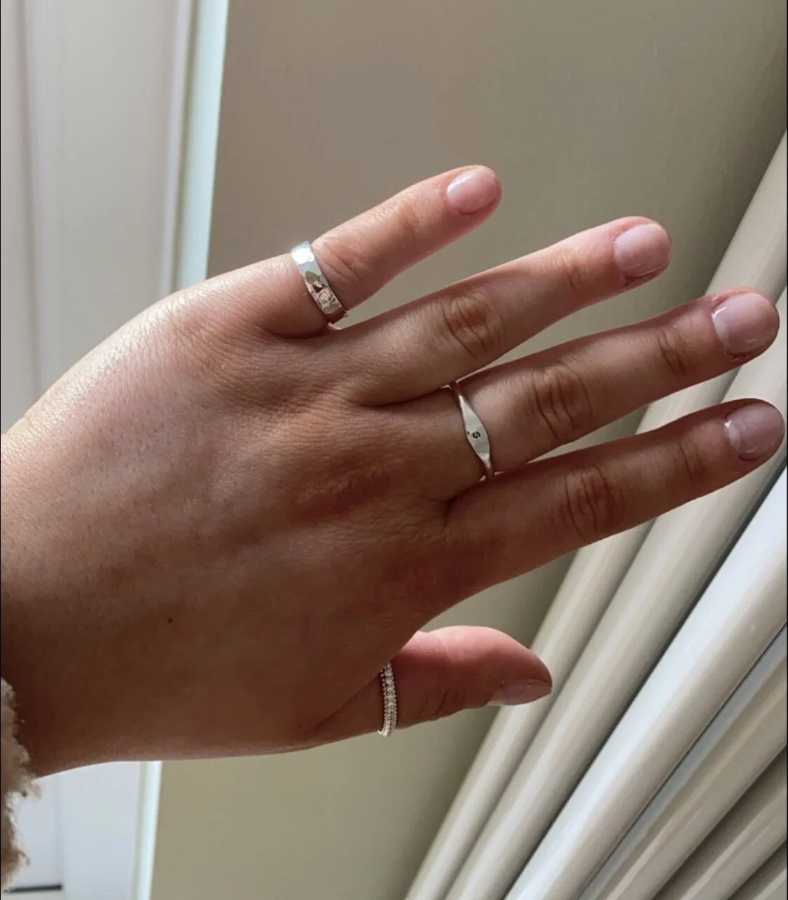 A hand wearing multiple silver rings with a light background.
