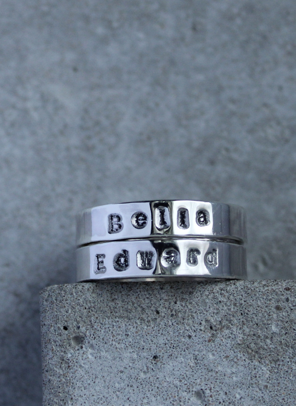 Two silver rings stacked with the names stamped on them.