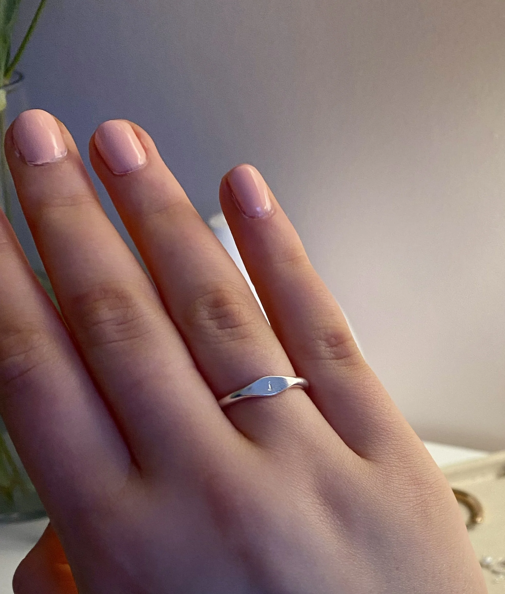 A close-up of a person's left hand displaying a silver ring with a curved design on the ring finger, with light pink nail polish on the nails.