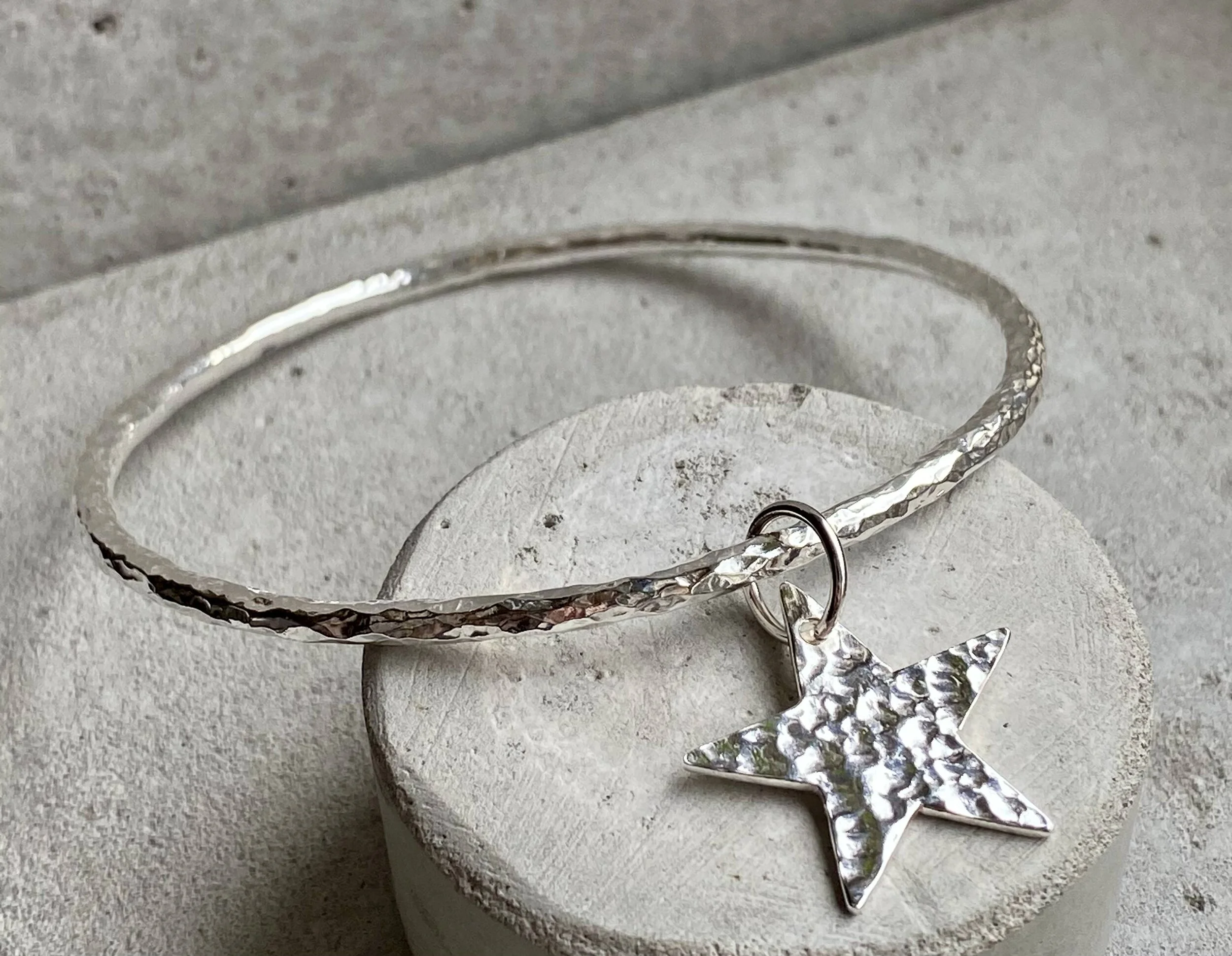 Silver bracelet with a star-shaped charm resting on a textured white surface.