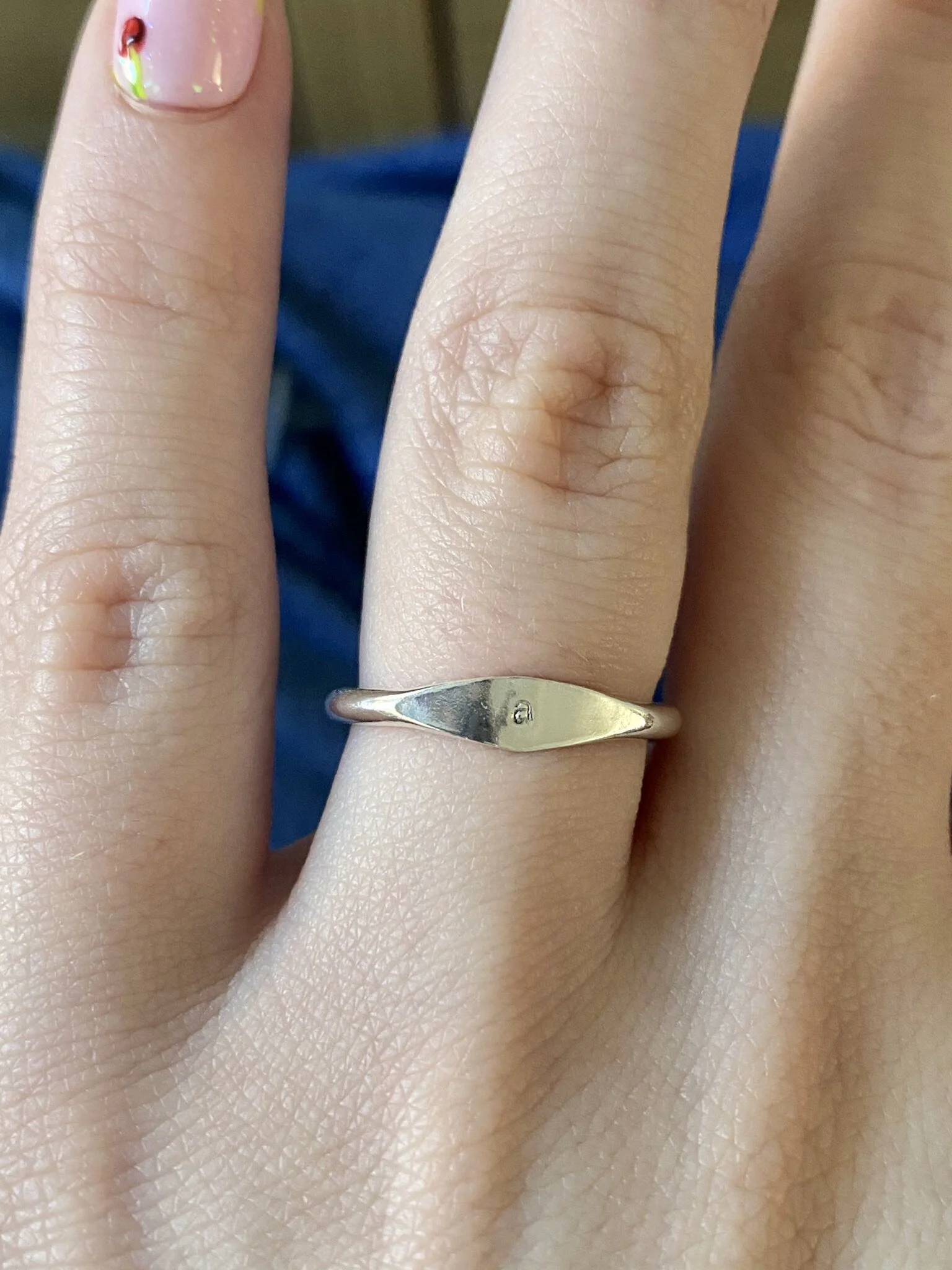 Close-up of a hand with a silver ring on the middle finger, featuring a small engraved letter 'g' and a nail with colorful nail art.