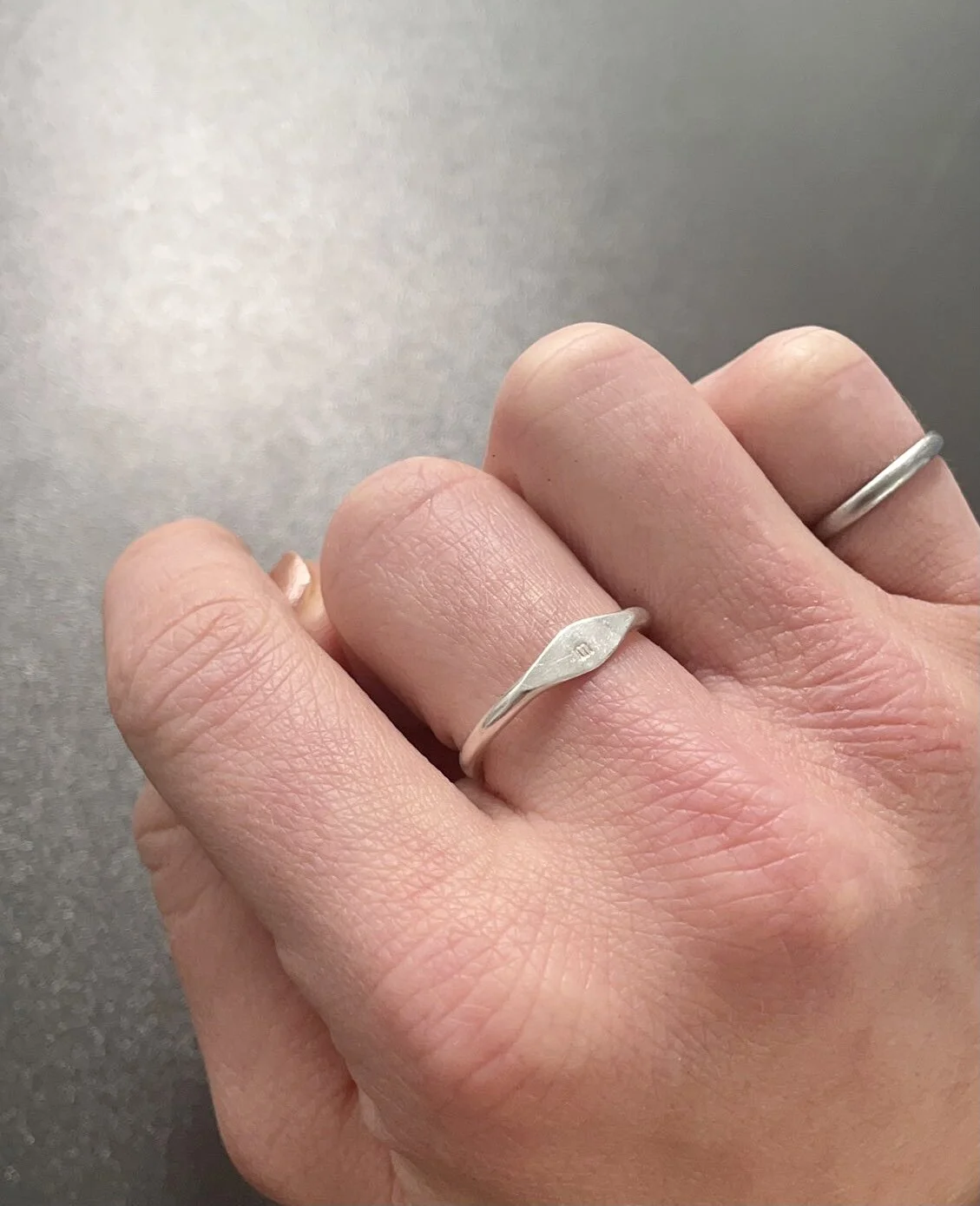 Close-up of a person's hand showing two silver rings on the index and middle fingers, with a textured background.