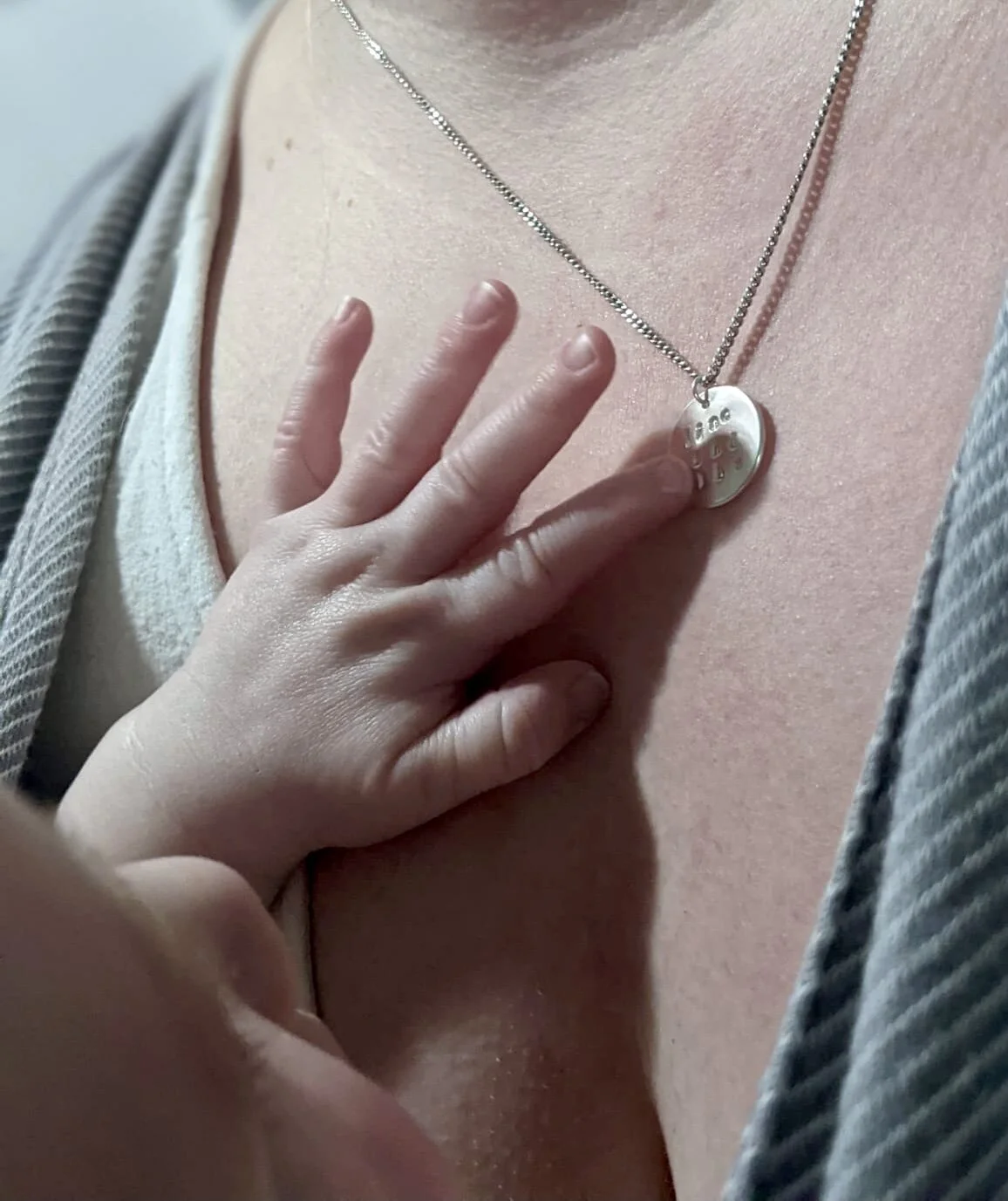A hand resting on a person's chest, near a silver necklace with a round pendant that has engraved patterns.