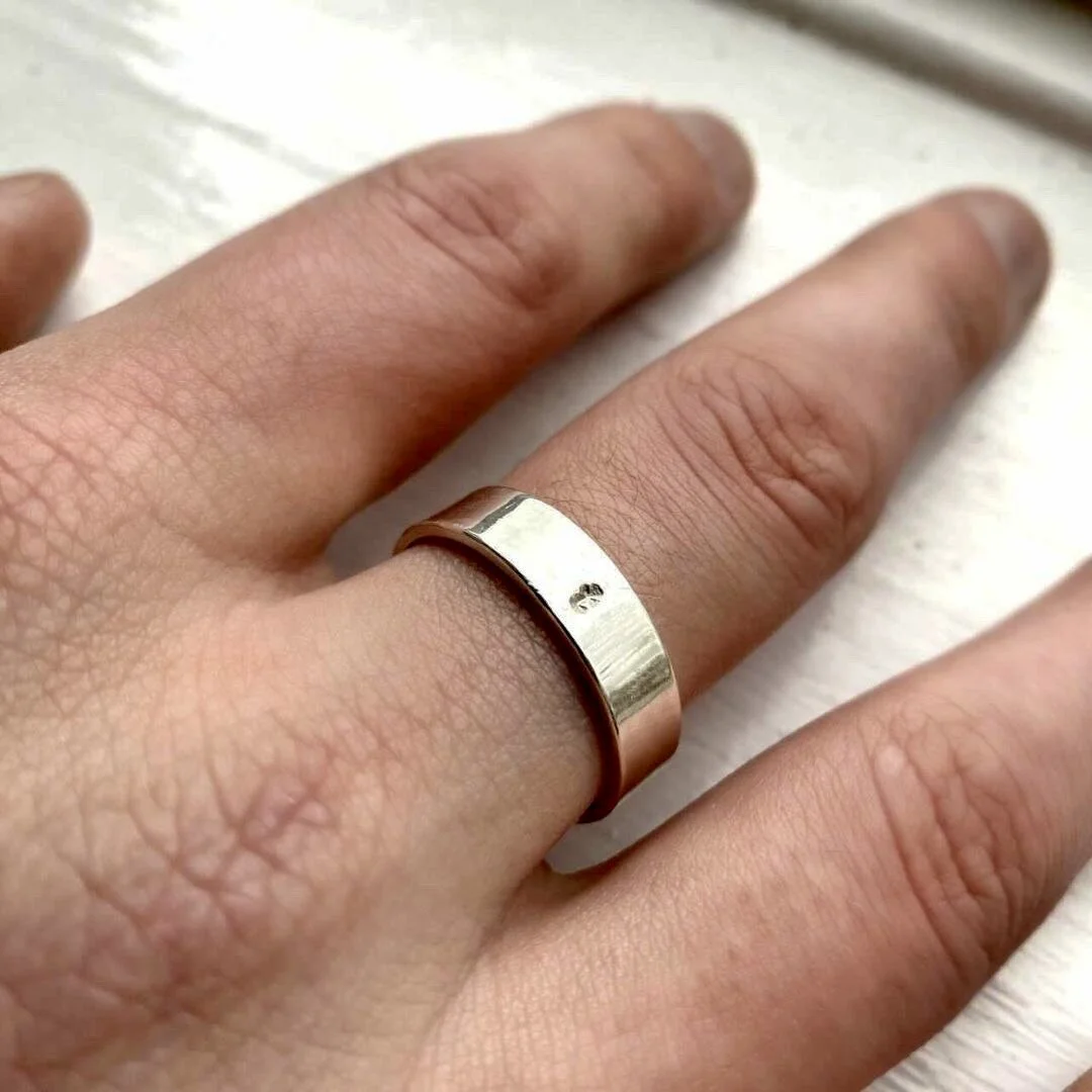 Close-up of a hand wearing a wide silver ring on the middle finger.