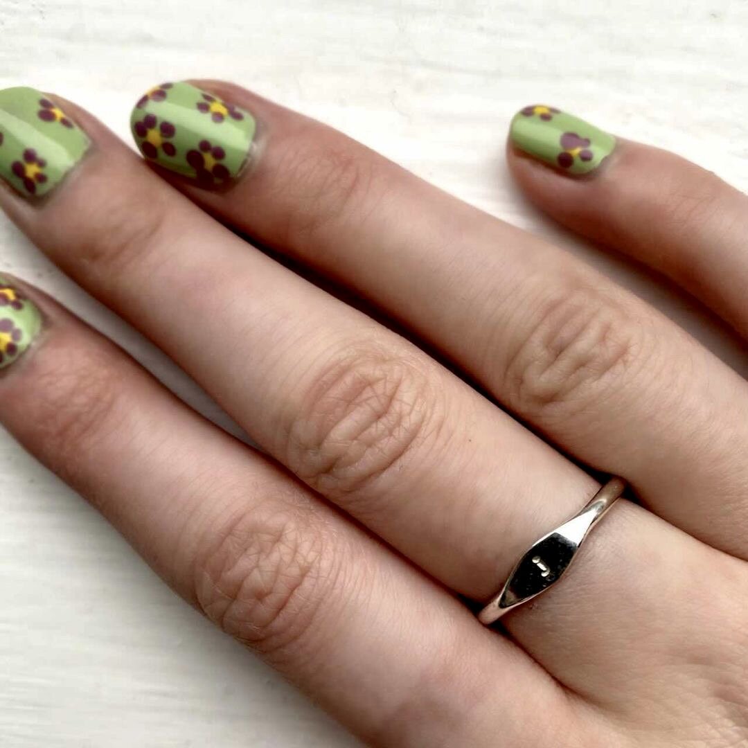 Close-up of a hand with floral nail art on painted nails and wearing a silver ring.