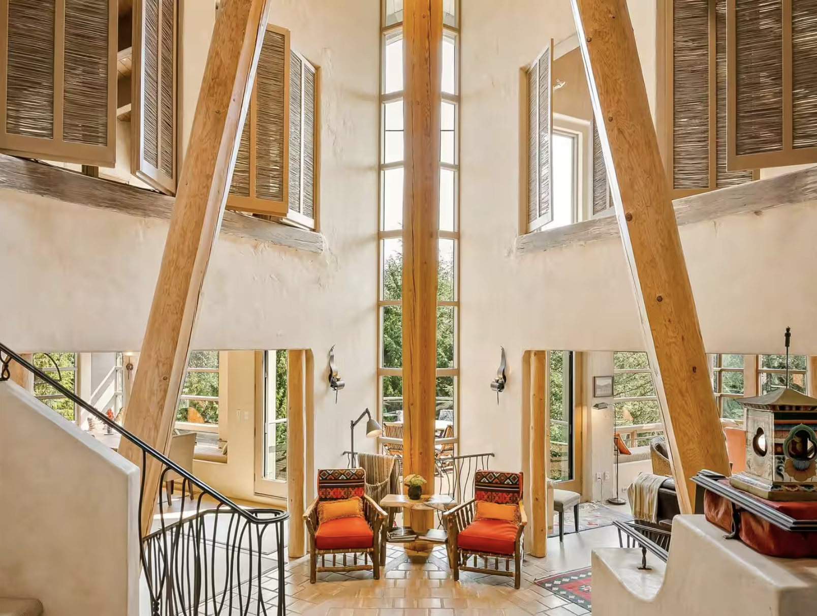 Interior view of a high-ceiling living room with large windows, wooden beams, and a seating area with two red-armchair and a small table.
