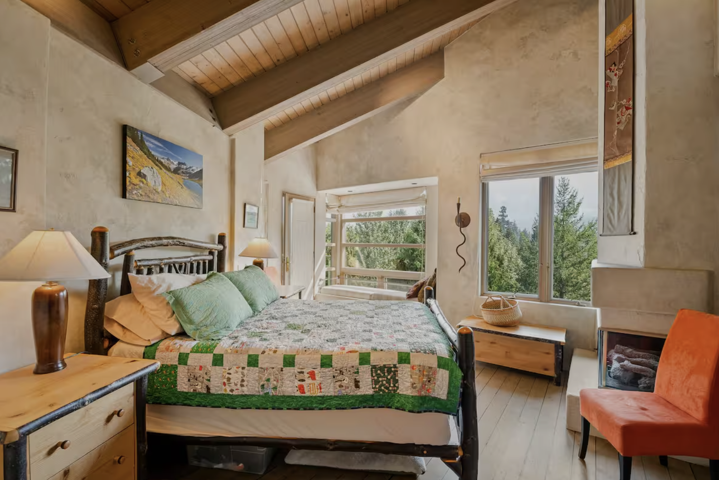 Cozy bedroom with a wooden canopy bed, adorned with green pillows and a quilt, in a room with high vaulted ceiling, large windows showing trees outside, and warm lighting from bedside lamps.