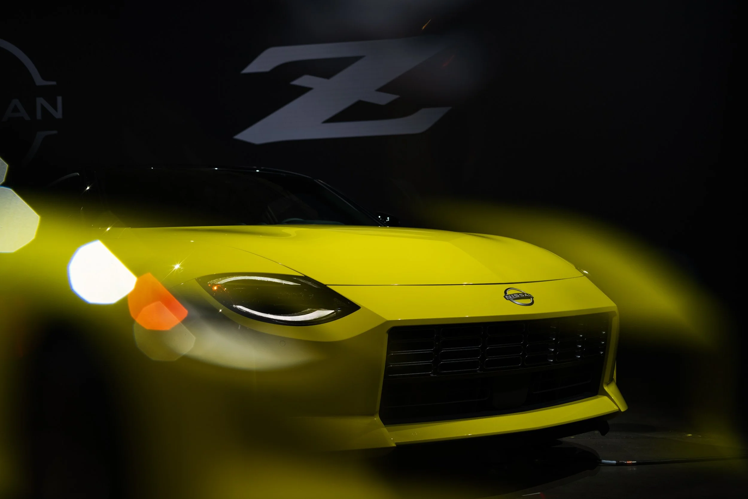Yellow Nissan sports car front view with logo on the hood, dark background.