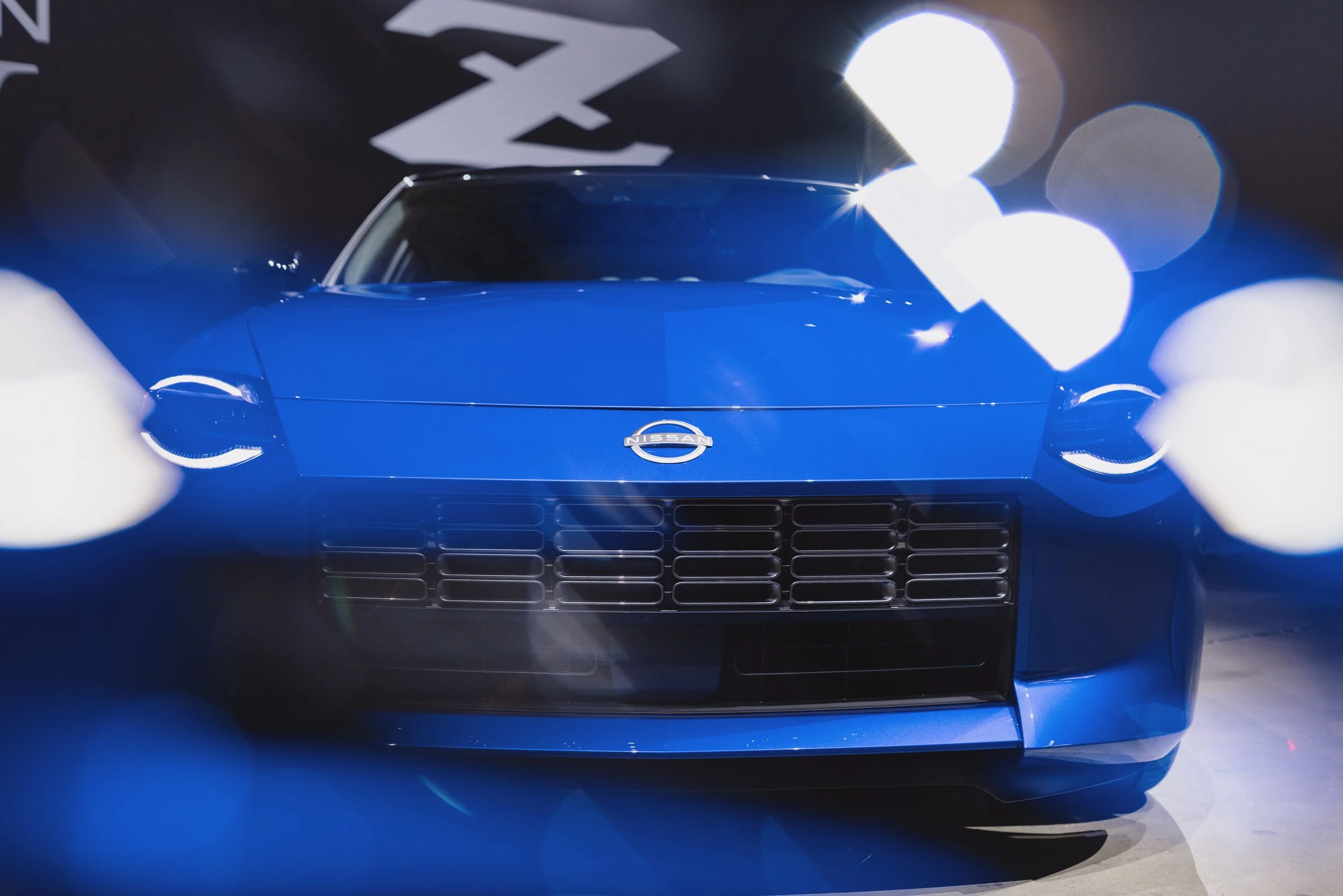 Front view of a blue sports car with a Nissan logo, highlighted by bright white lens flares.
