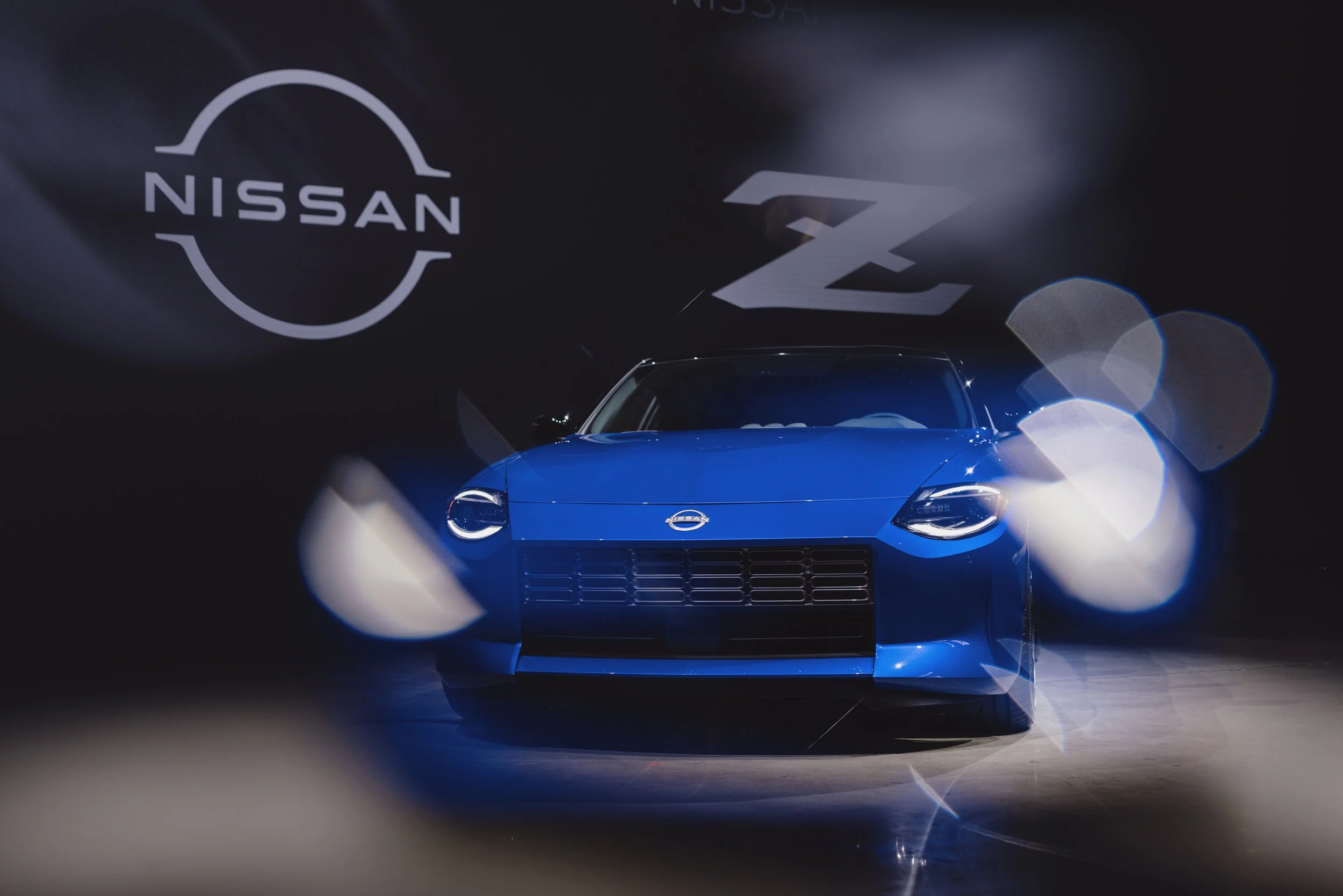 Blue Nissan Z car under spotlights with Nissan and Z logos in the background.