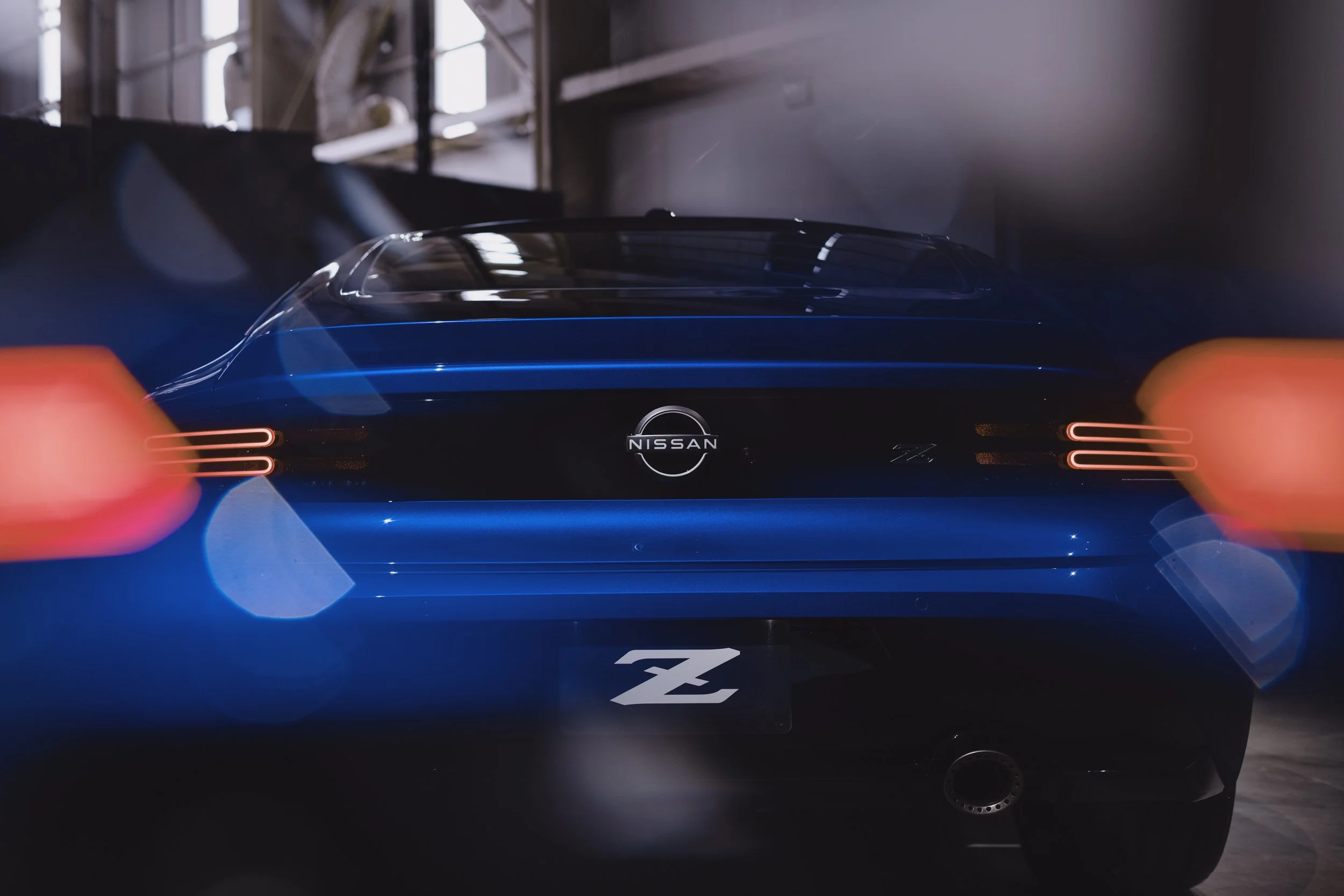 Rear view of a blue Nissan sports car with illuminated taillights in a dimly lit environment.