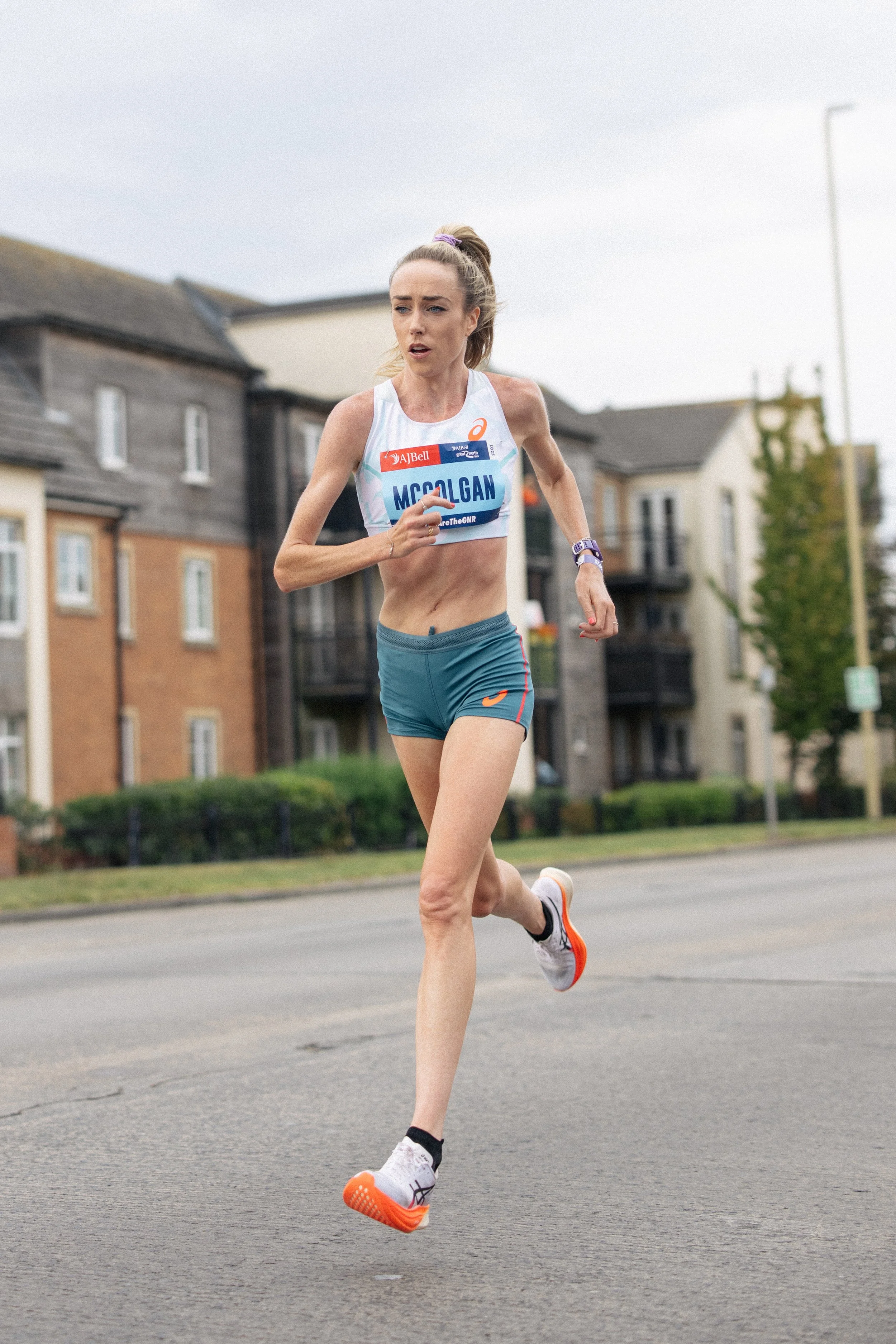 A female marathon runner in athletic gear running on a street in an urban area with residential buildings in the background.