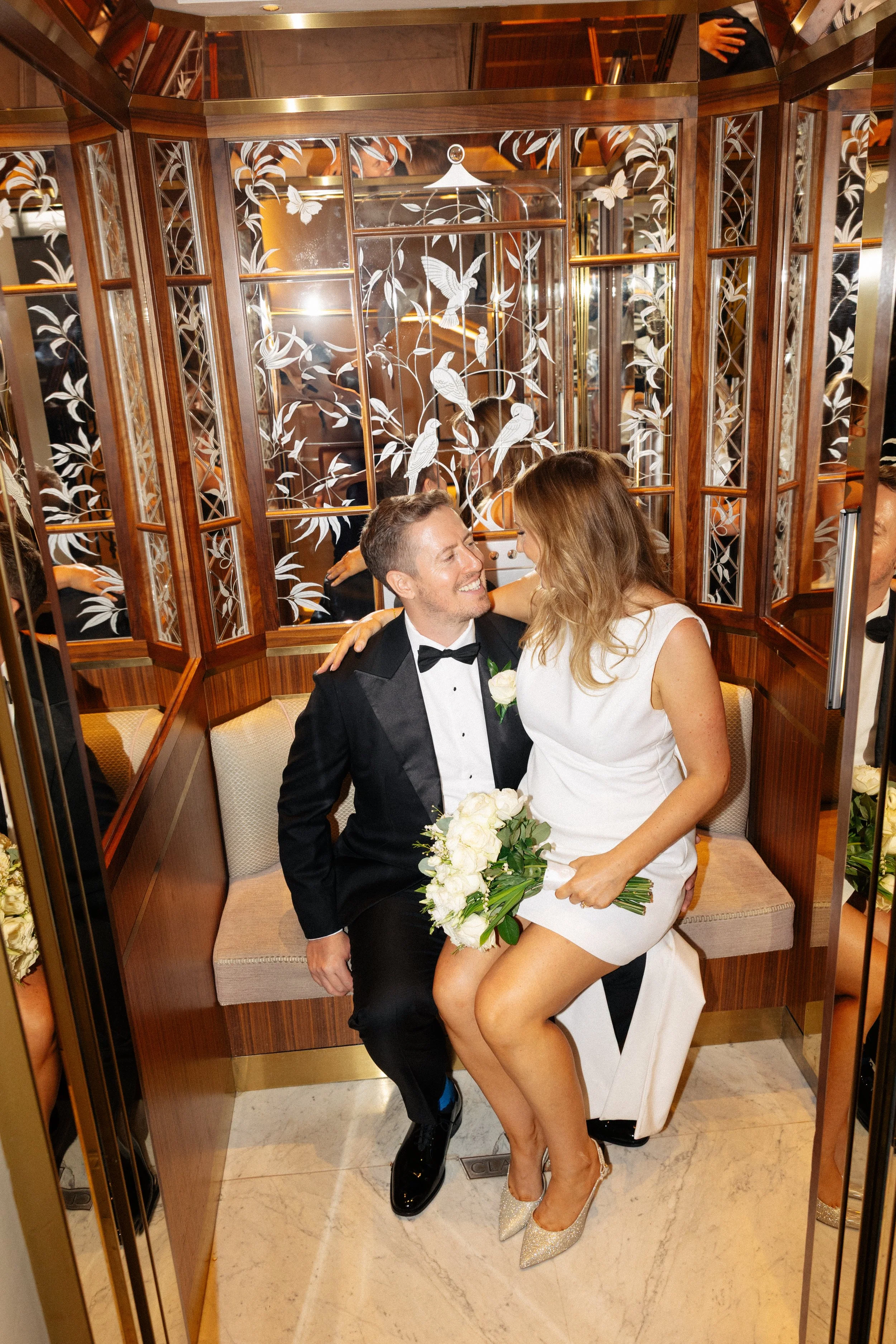 A bride sits on her grooms leg in the lift at Claridges 