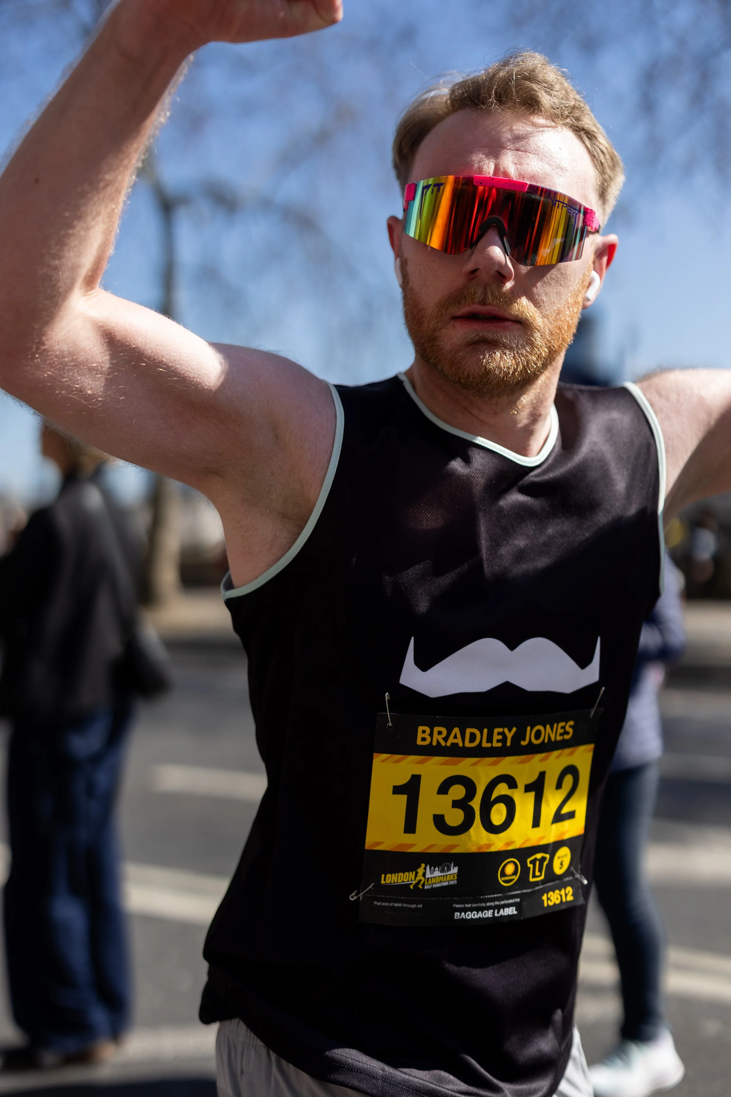 A man wearing sunglasses and a black running tank top with a bib number 13612, participating in a marathon or race event outdoors on a sunny day.