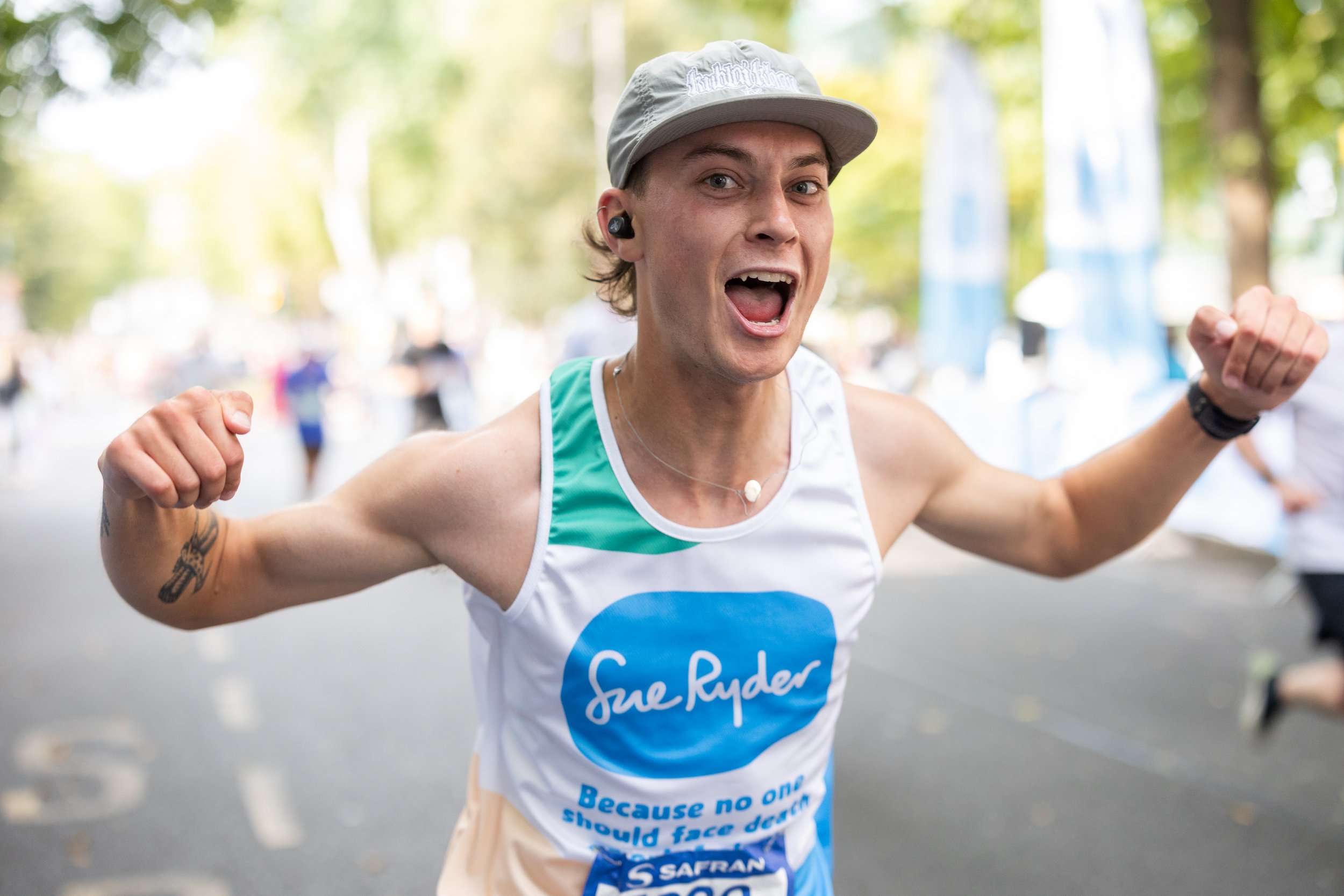 A male half marathon runner in a tank top and gray cap smiling and flexing his arms.
