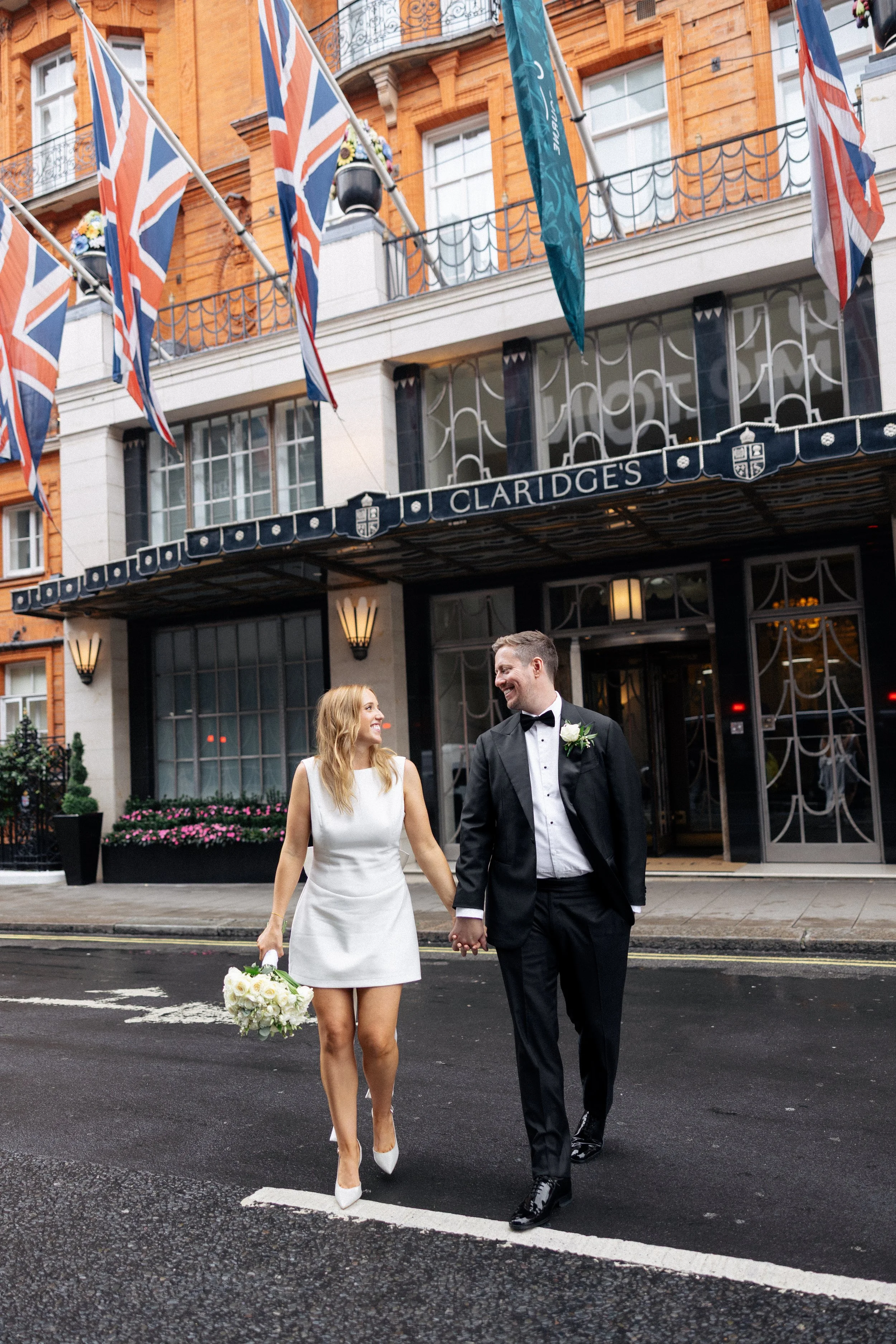 A bride and groom walk across the road outside Claridges in London