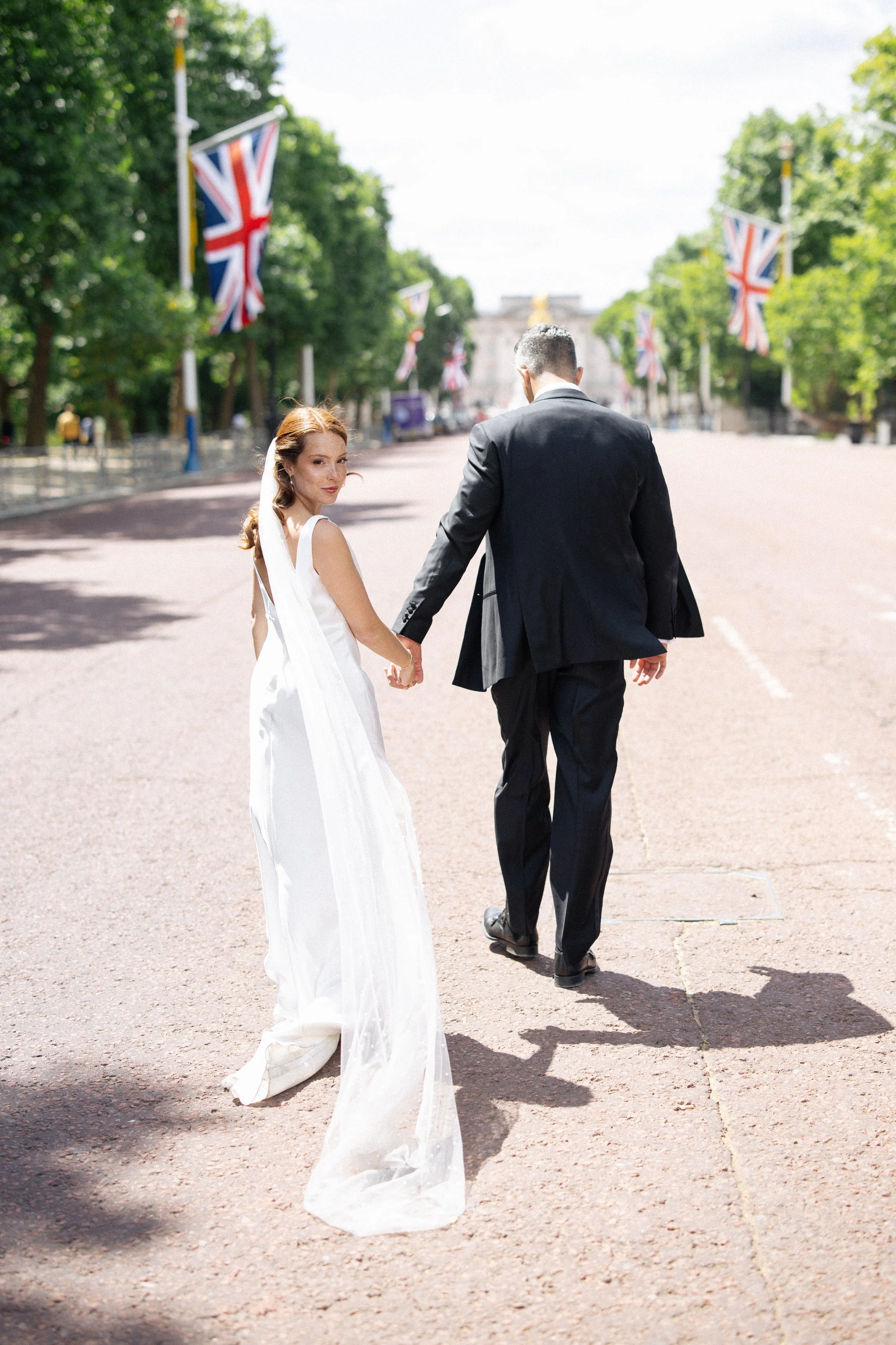 A bride looks over her shoulder as her groom leads her down the Mall towards Buckingham Palace in London