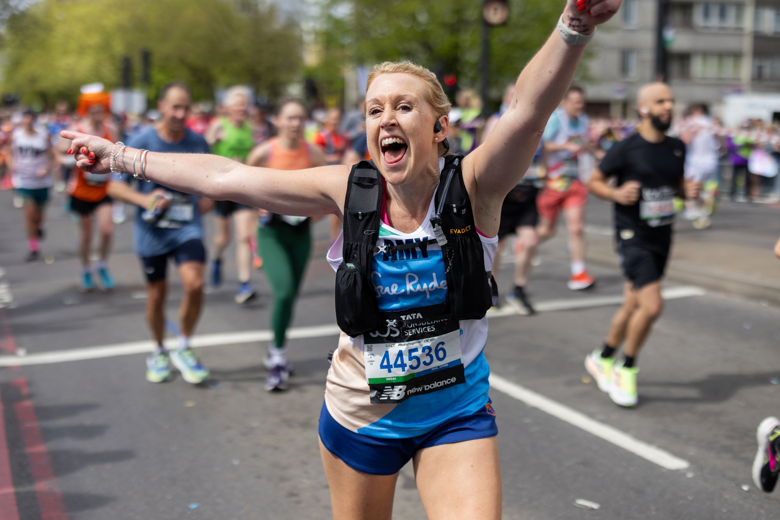 A woman cheering with arms raised during a marathon, surrounded by other runners on a city street.