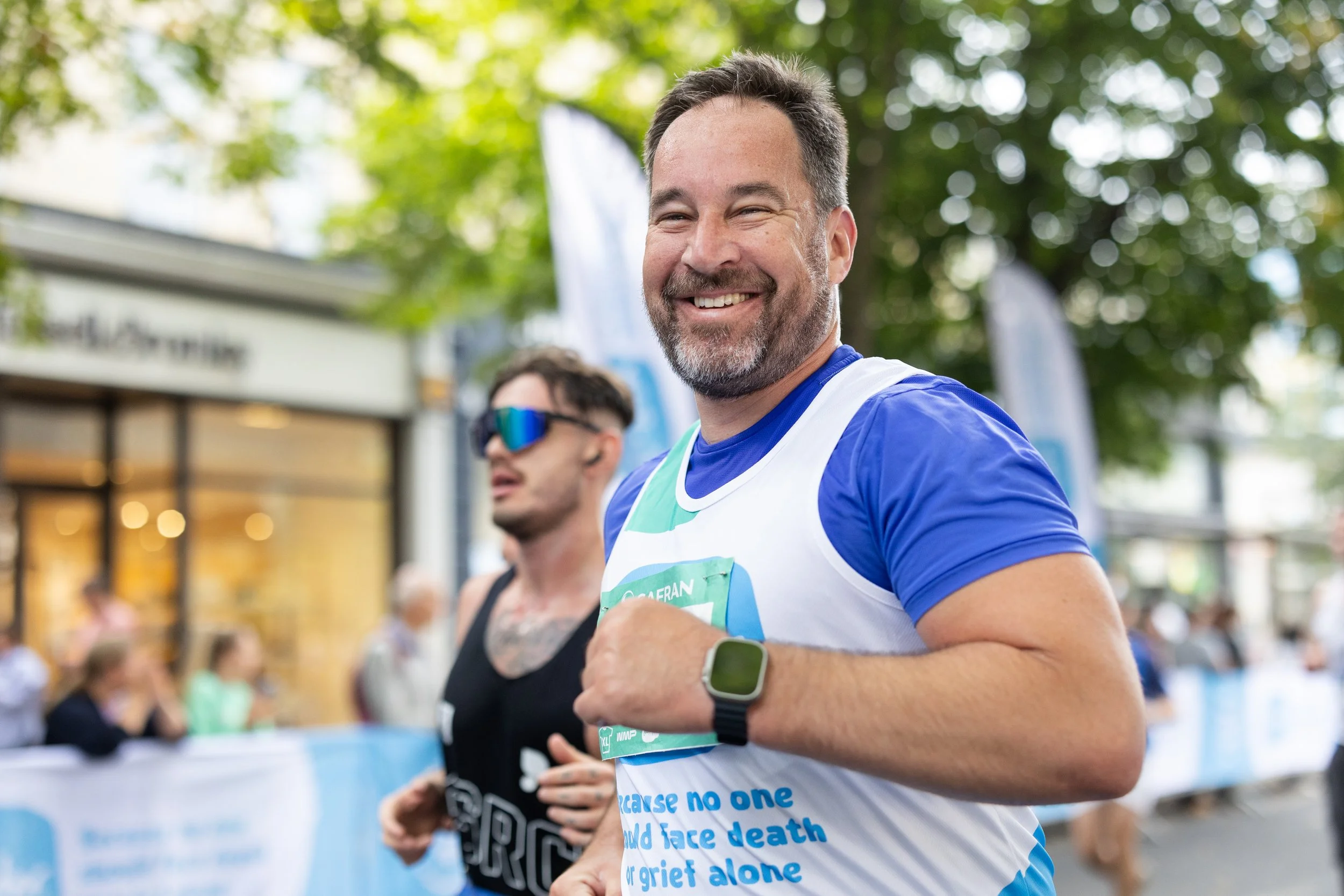 A man smiles while running the Cheltenham Half Marathon for Sue Ryder.