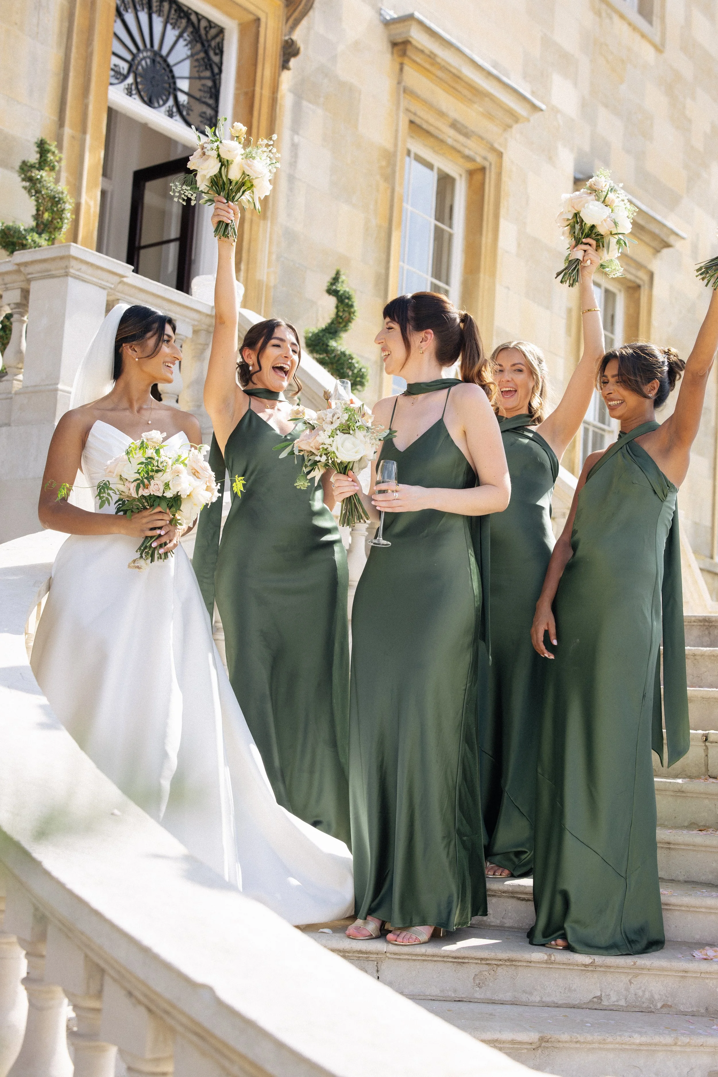 A bride and her bridesmaids cheer on the steps outside Botleys Mansion