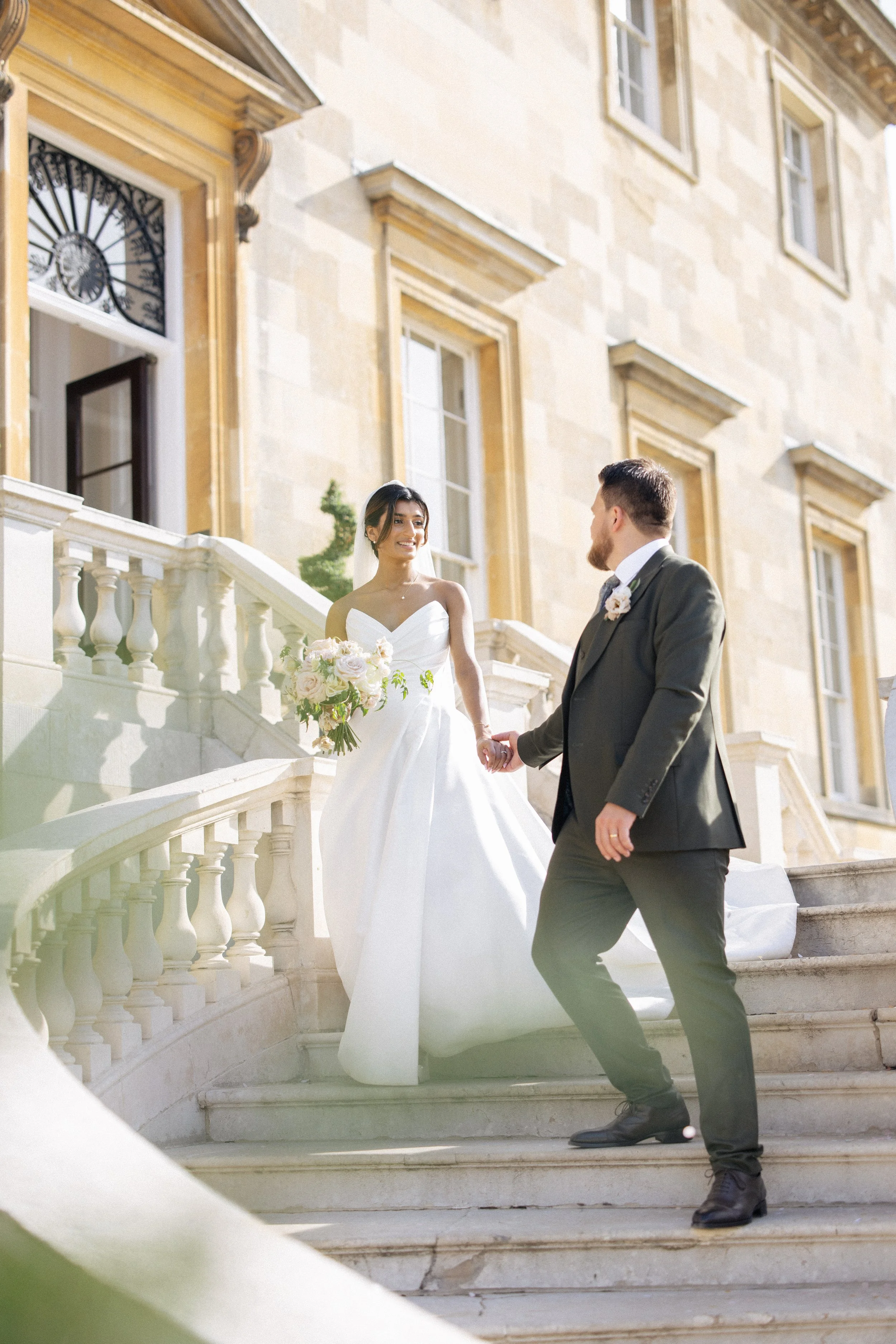 A bride and groom walk down the steps of Botleys Mansion after their wedding ceremony