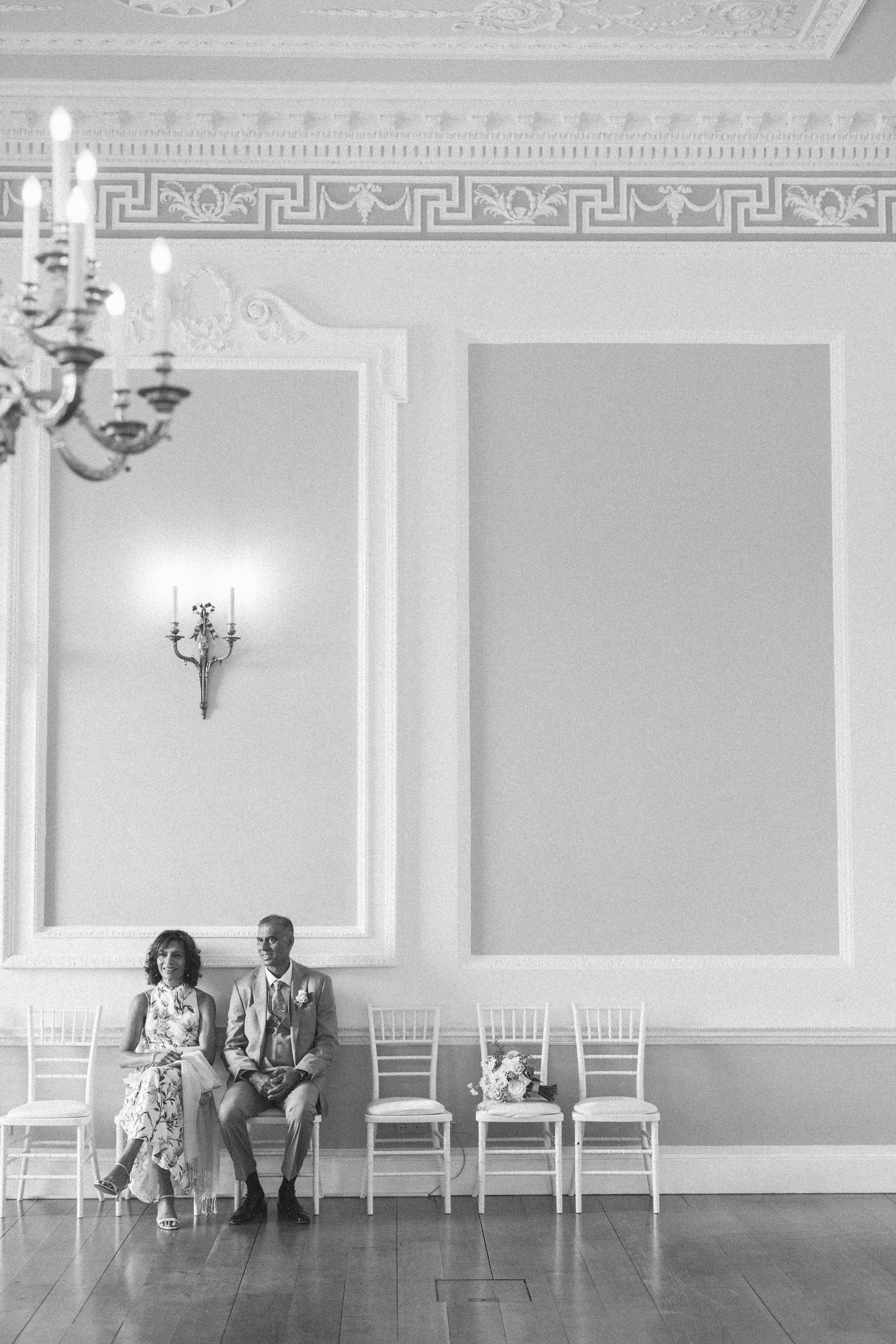 A mother and father of the bride sit quietly alone waiting for the wedding ceremony at Botleys Mansion to begin