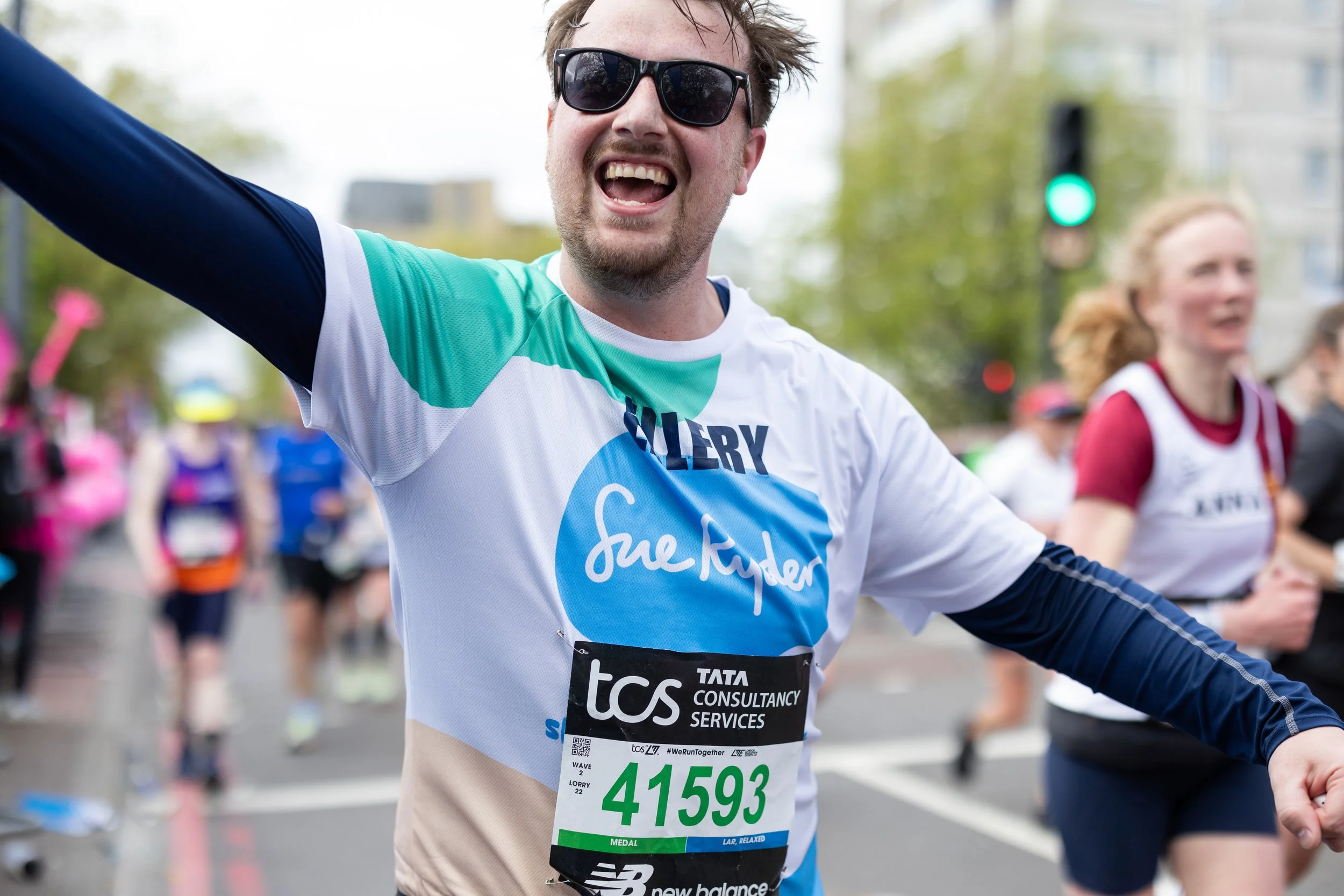 A smiling male marathon runner wearing sunglasses and race bib 41593, raising his arm in celebration during a race.