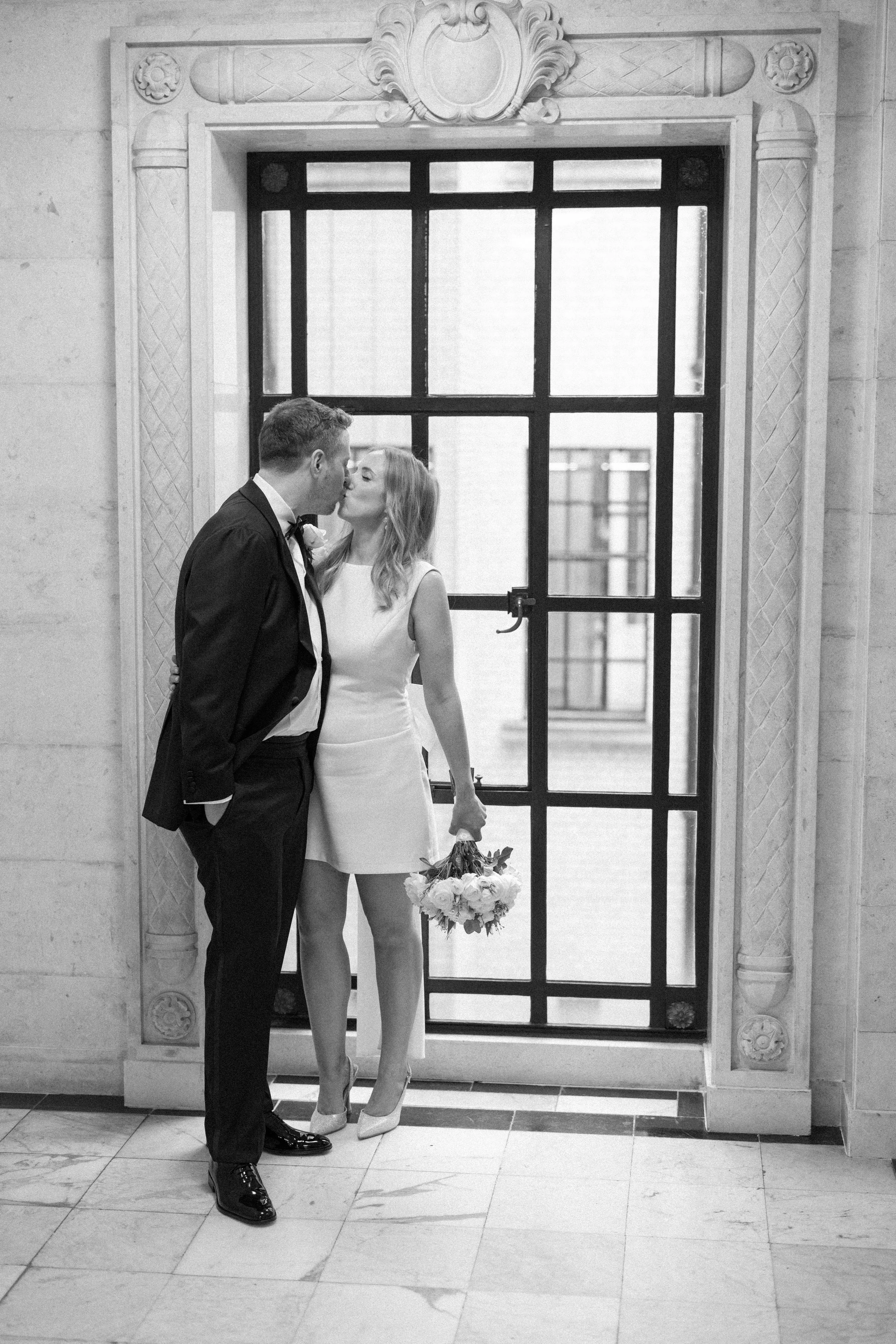 A couple kiss in front of a window in Marylebone Town Hall after their wedding ceremony