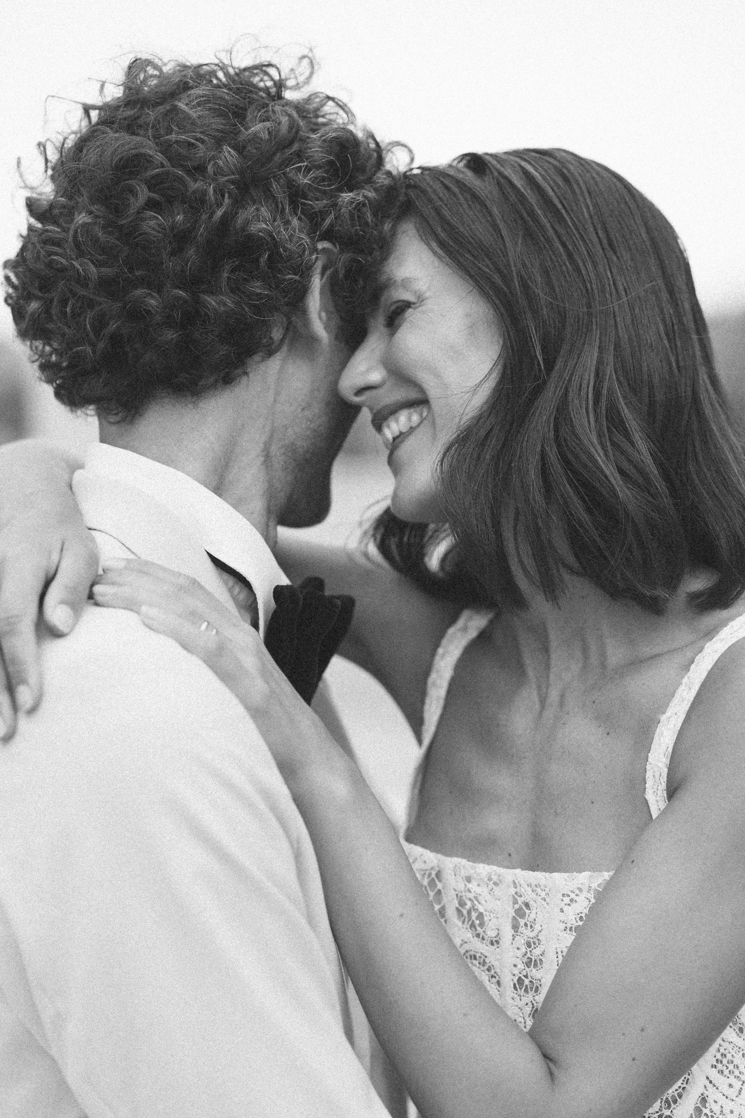 A bride cuddles up to her groom and puts her arm around him and smiles