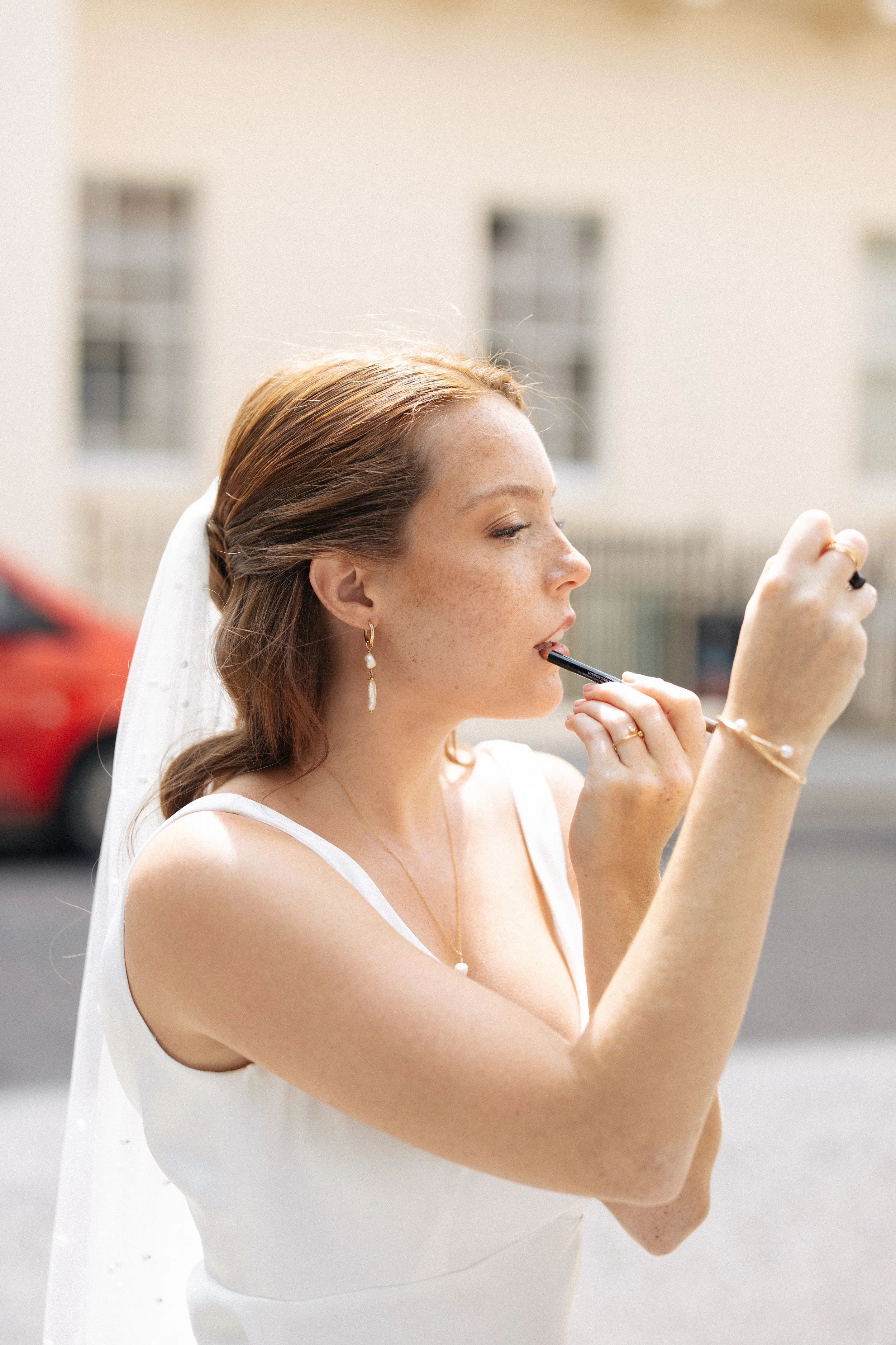A bride reapplies make up on the side of the road before her wedding portraits in Pall Mall in London