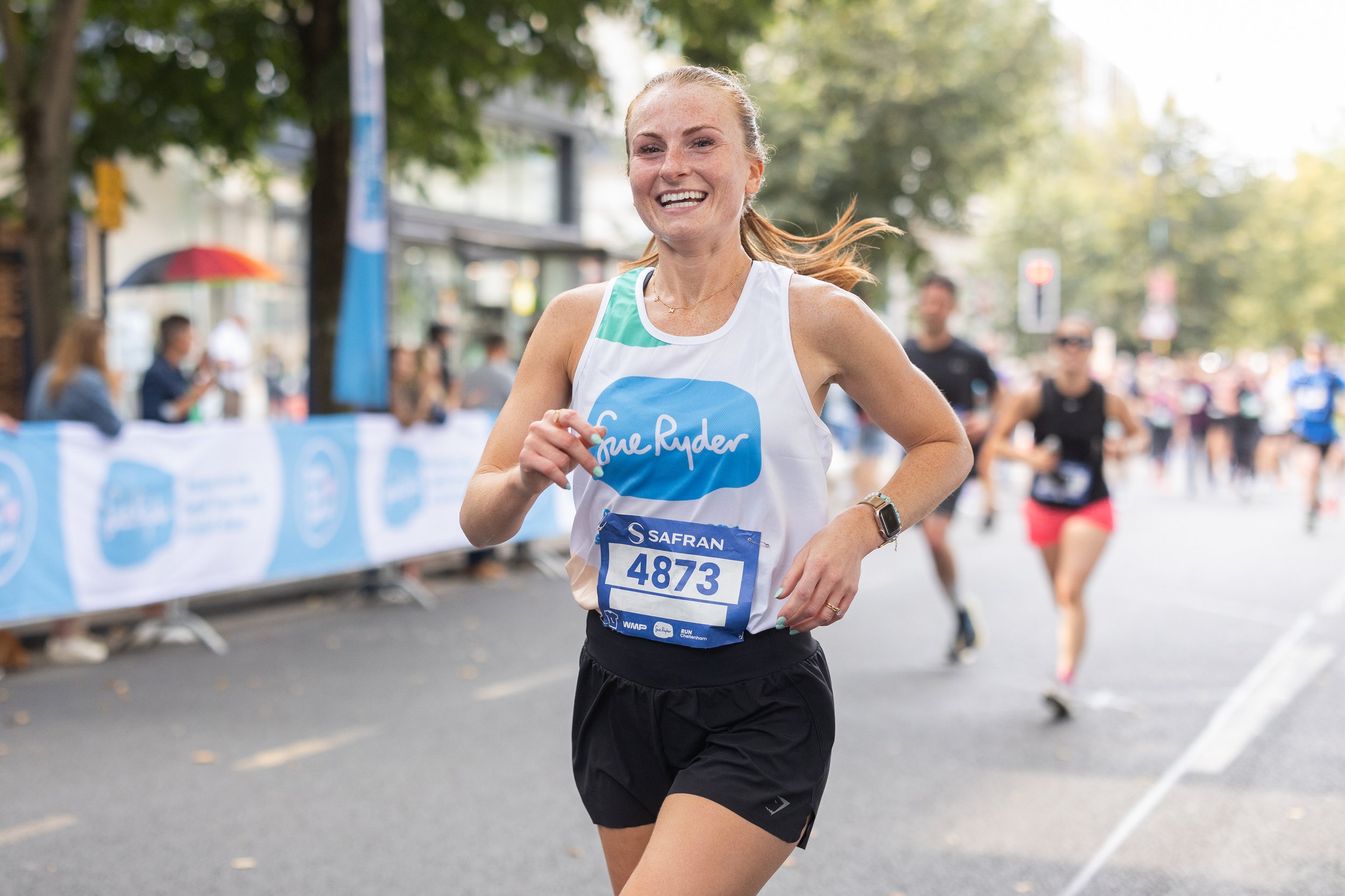 A woman smiling as she is running the Cheltenham Half Marathon for Sue Ryder.