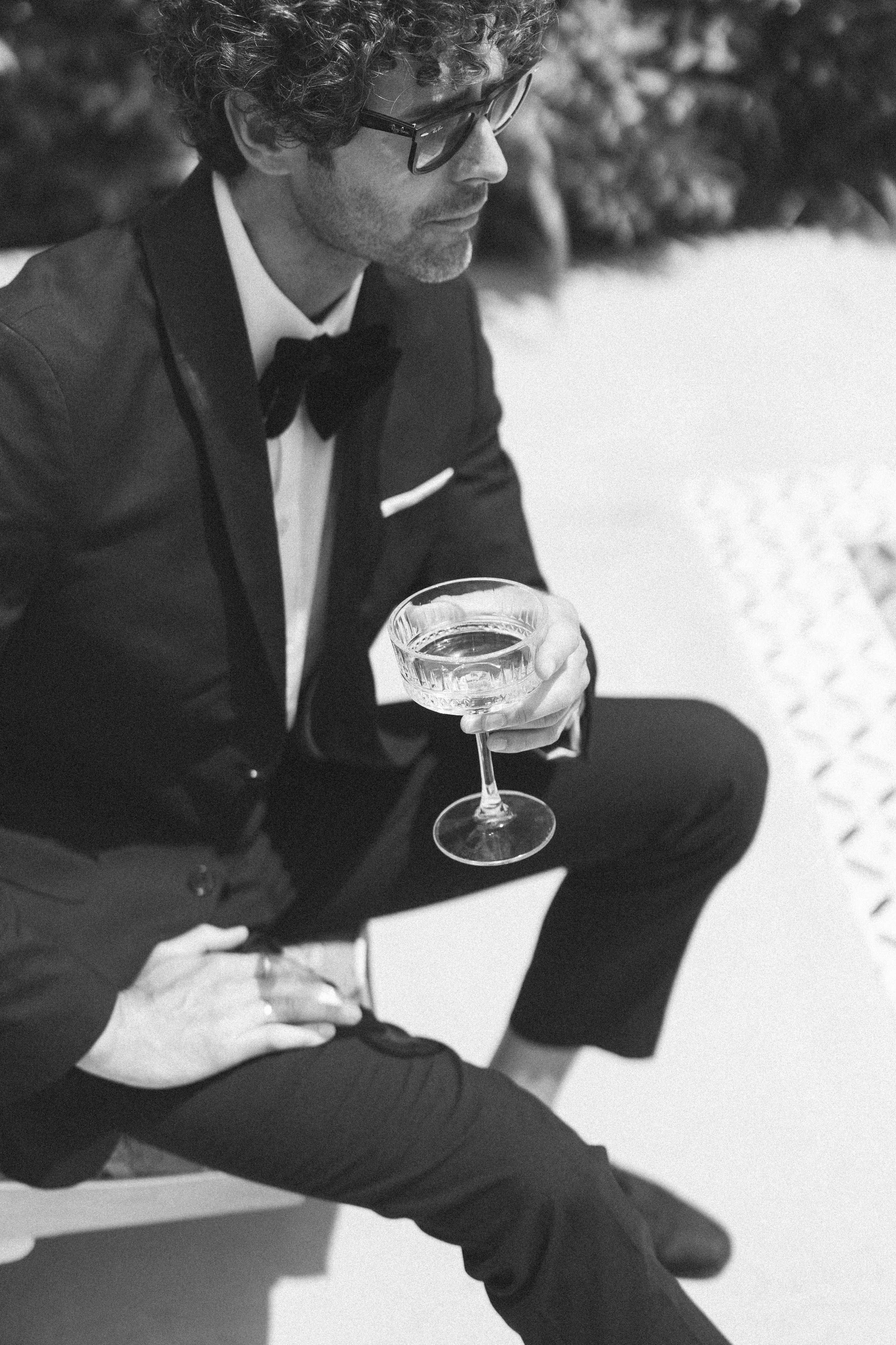 A groom sits with a glass of champagne before his wedding at Braccialieri in Sicily
