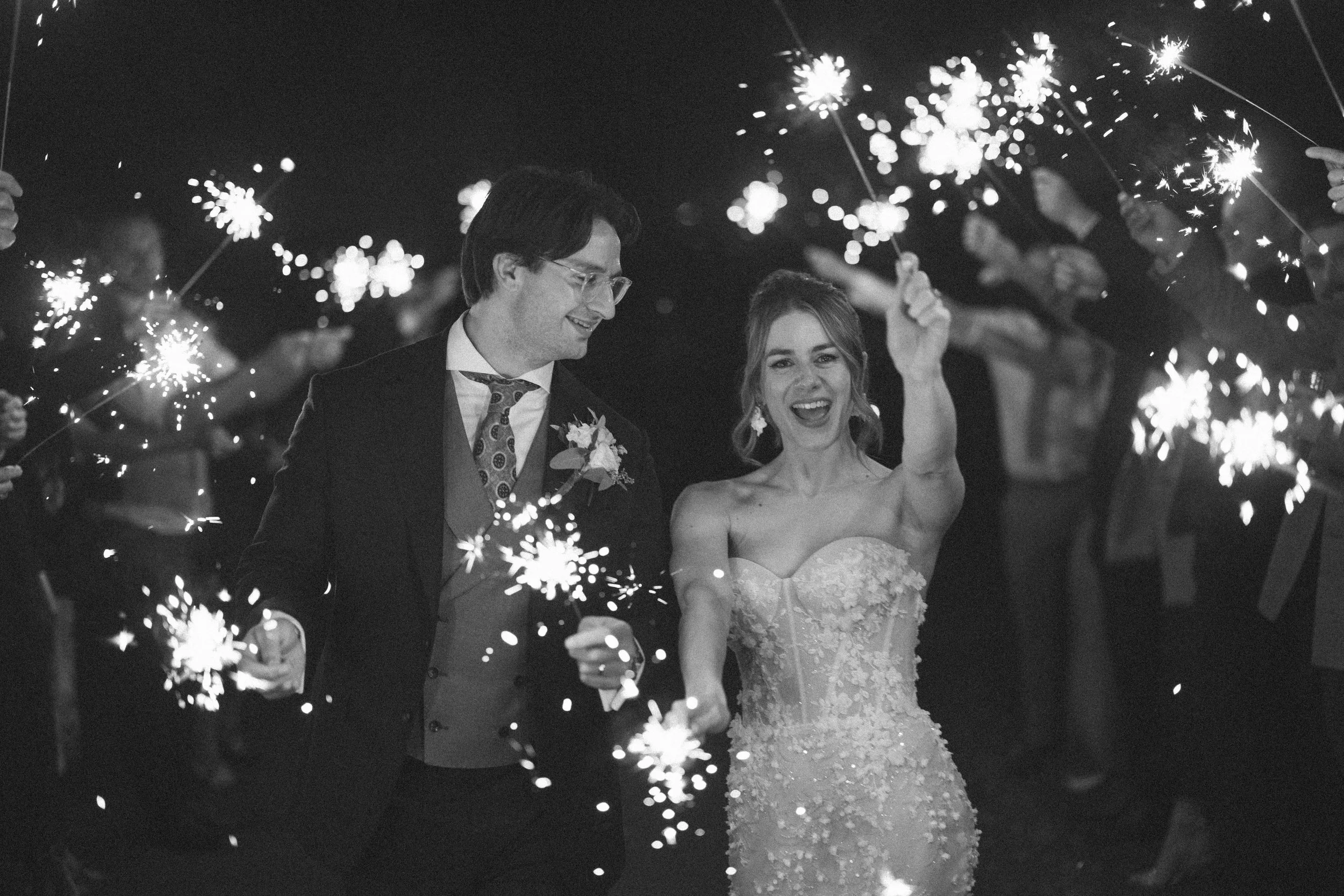 A bride and groom wave sparklers with friends at the Orangery Maidstone