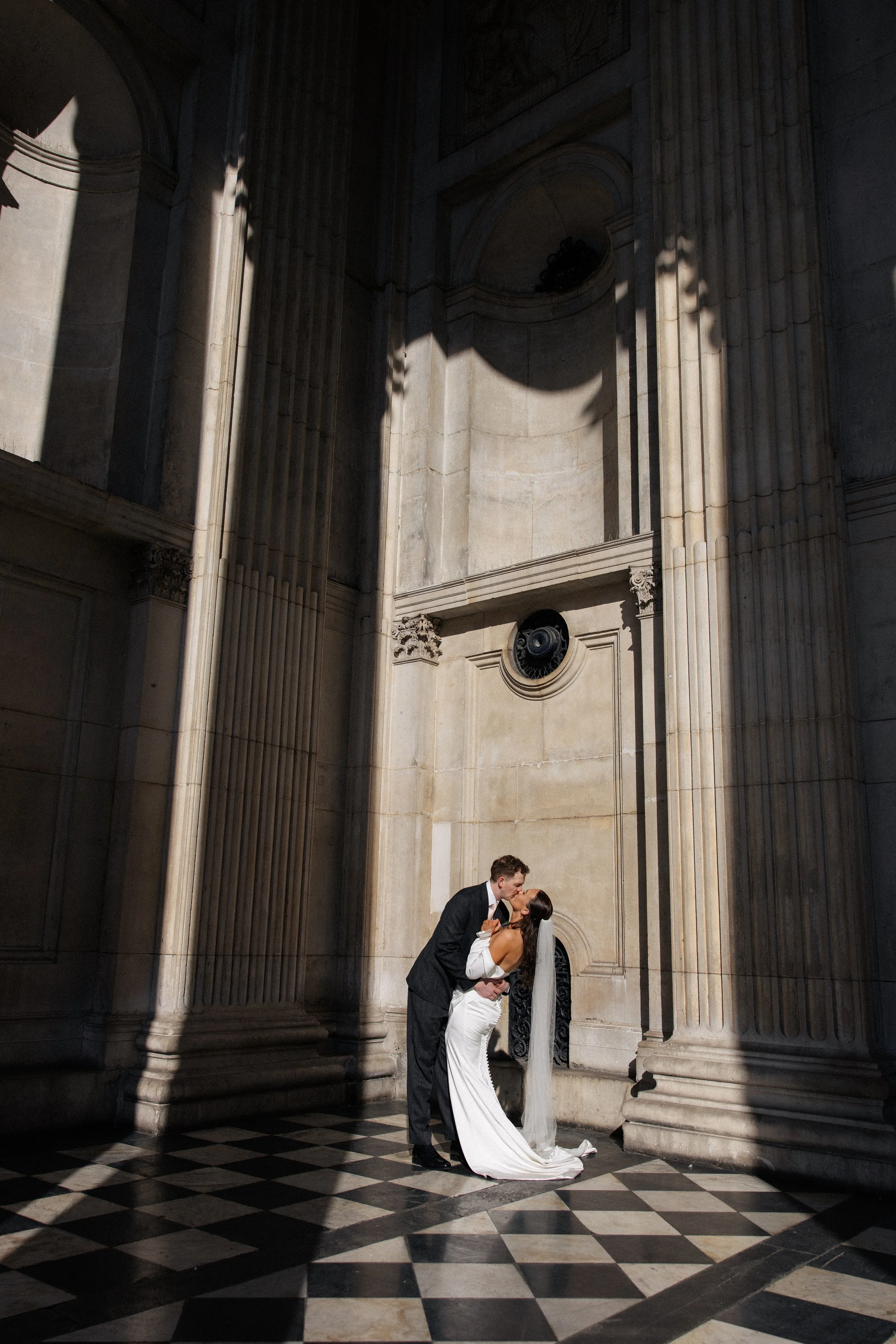 A bride and groom kiss in the sunshine on the steps of St Pauls Cathedral after their wedding