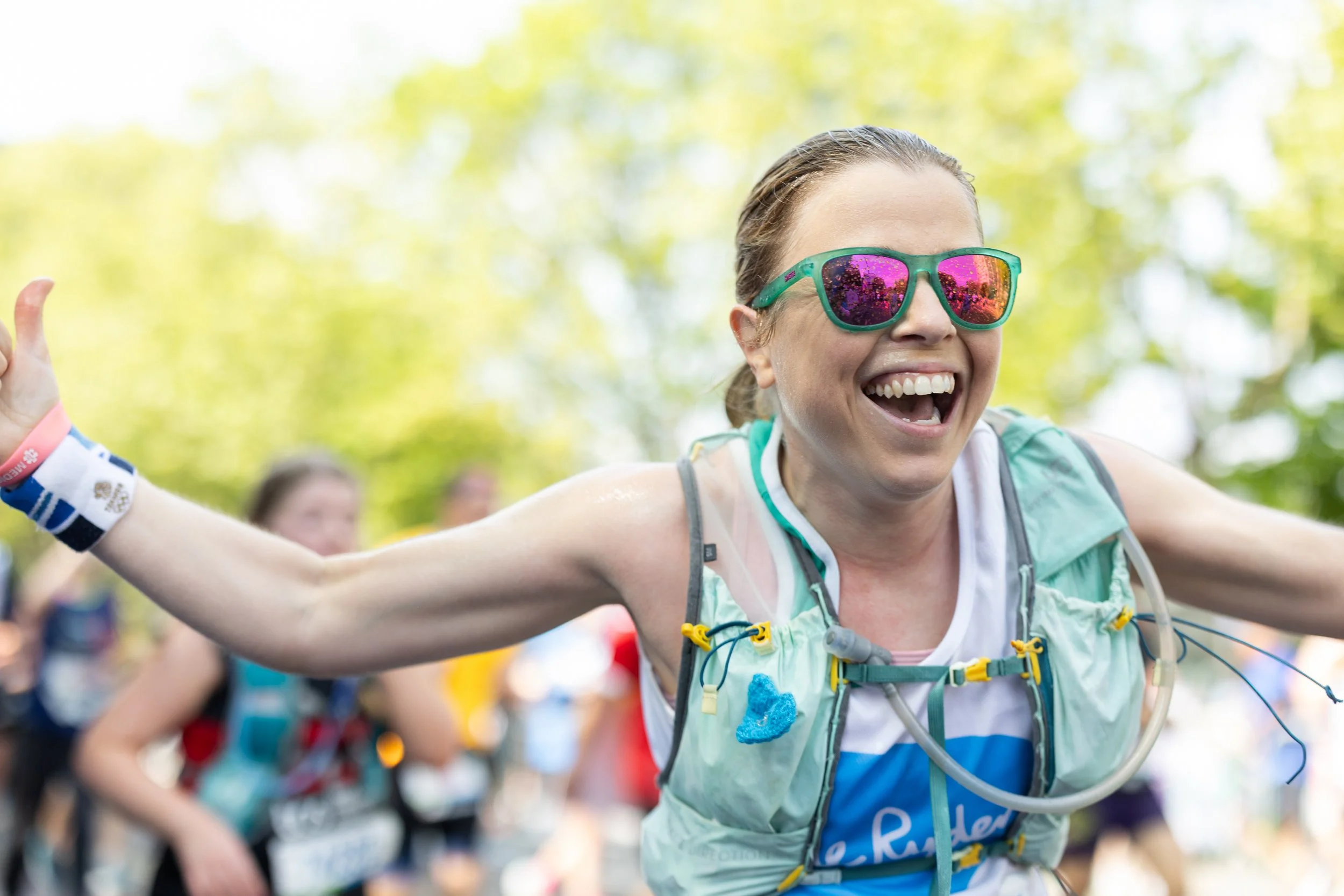 Woman in sunglasses and running gear celebrating during a race in a park.