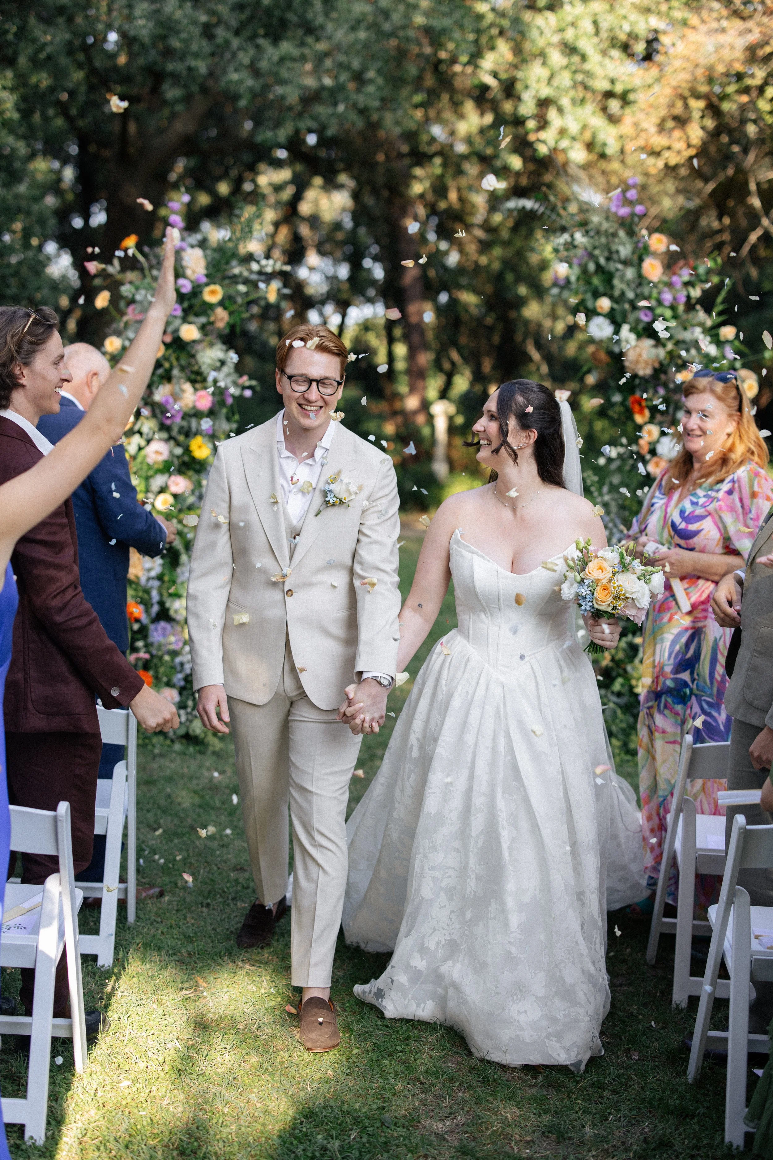 A bride and groom walk through friends throwing confetti after their ceremony at Villa Giulia in Fano, Italy