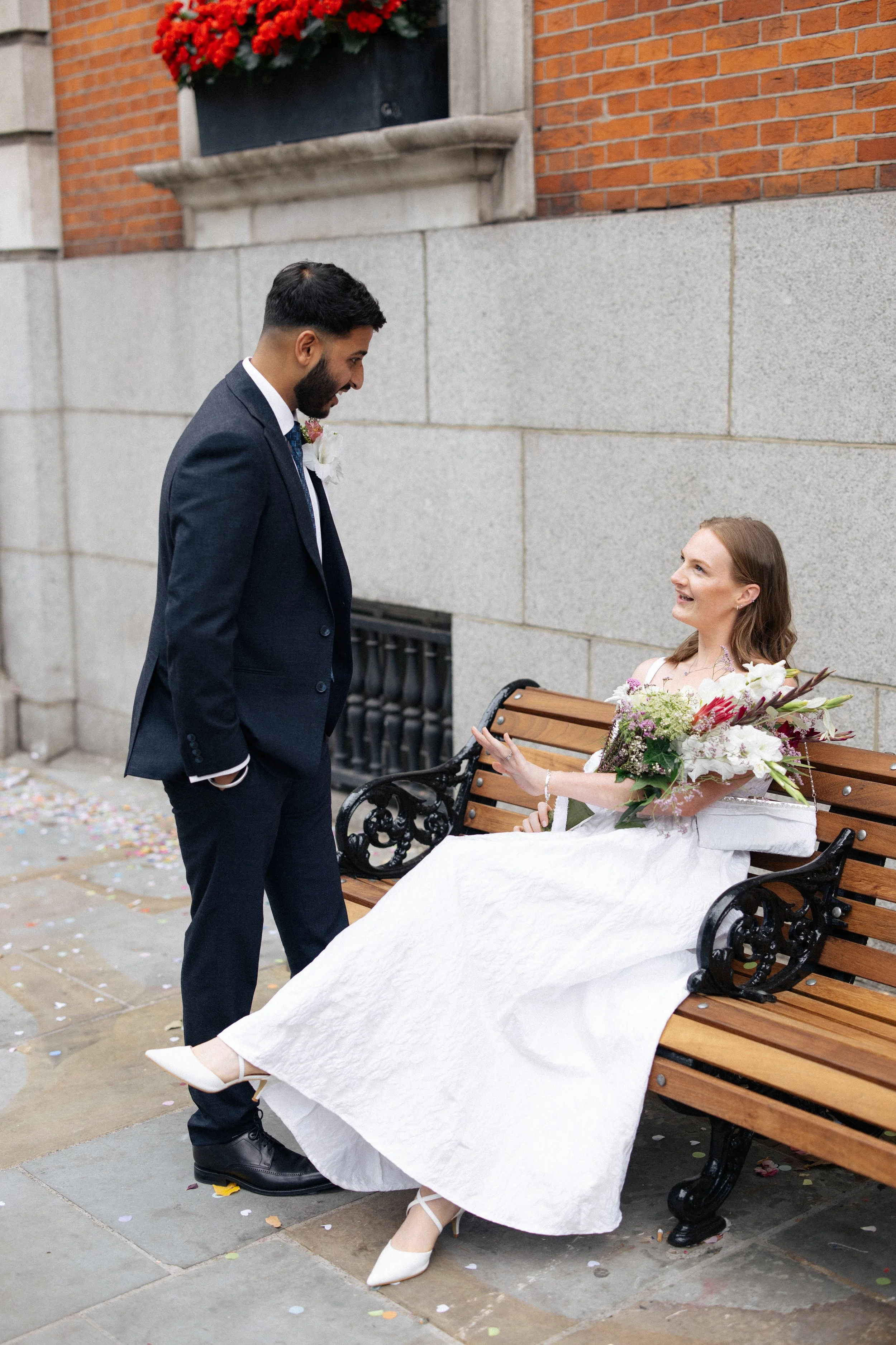 A bride sits on a bench with her groom beside her at Chelsea Old Town Hall