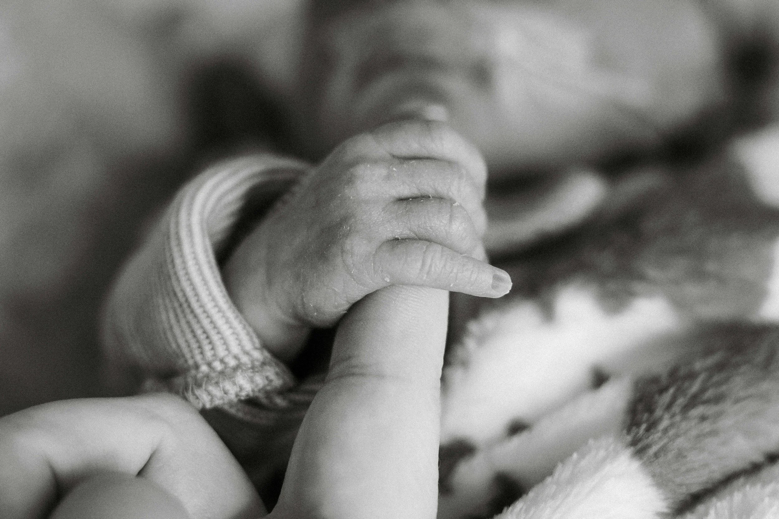 Close-up of a baby’s hand holding an adult’s finger, in black and white.
