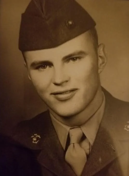 A black-and-white photograph of a young man, Sam Haycraft  in 1950s US Marine Corps uniform, wearing a cap, tie, and dress shirt, with a slight smile. Semper Fi