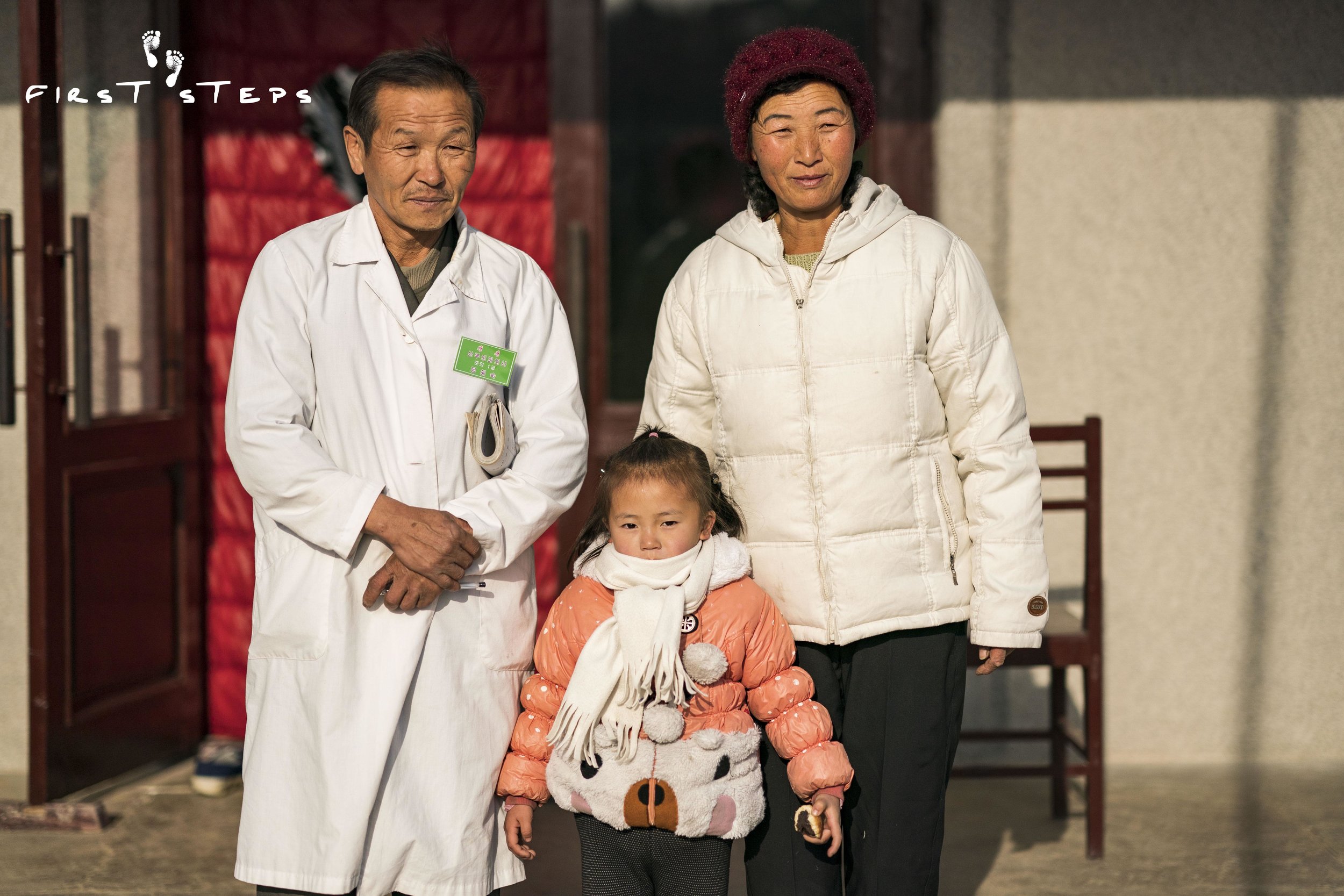 Dr. Kim Sun-Man, director of the Shinmi Policlinic, standing with his wife Mrs. Ri Yon-Ok and their four-year-old grand-daughter Na-Rye.