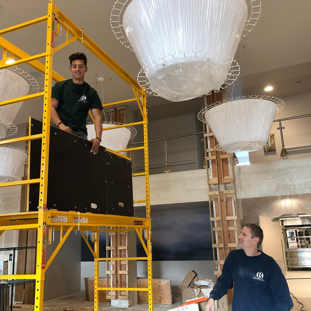 Two men working with scaffolding and lighting fixtures in an indoor space.