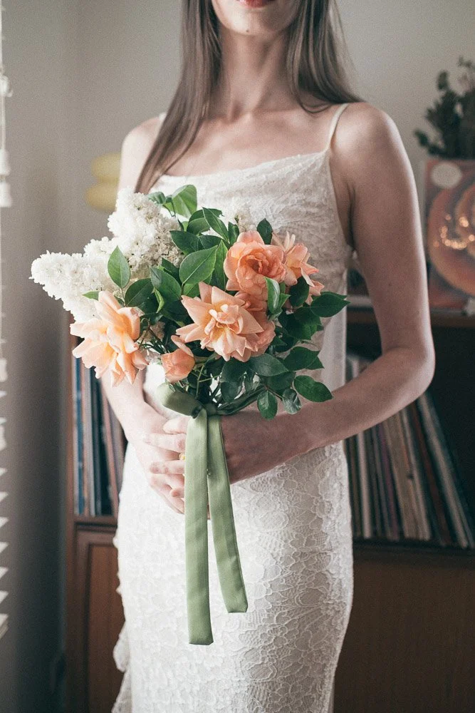 , BRIDE POSIN WITH FLOWERS NEXT TO A WINDOW