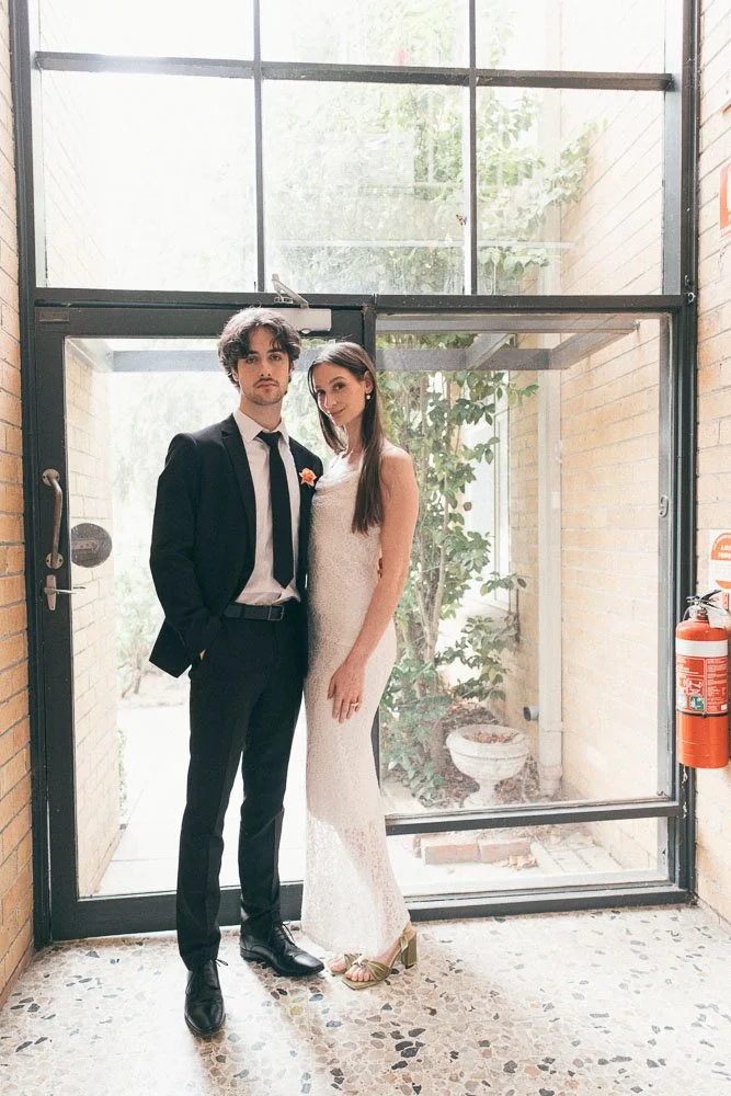 , BRIDE AND GROOM CASUALLY POSING INSIDE AN APARTMENT NEXT TO HUGE GLASS WINDOWS
